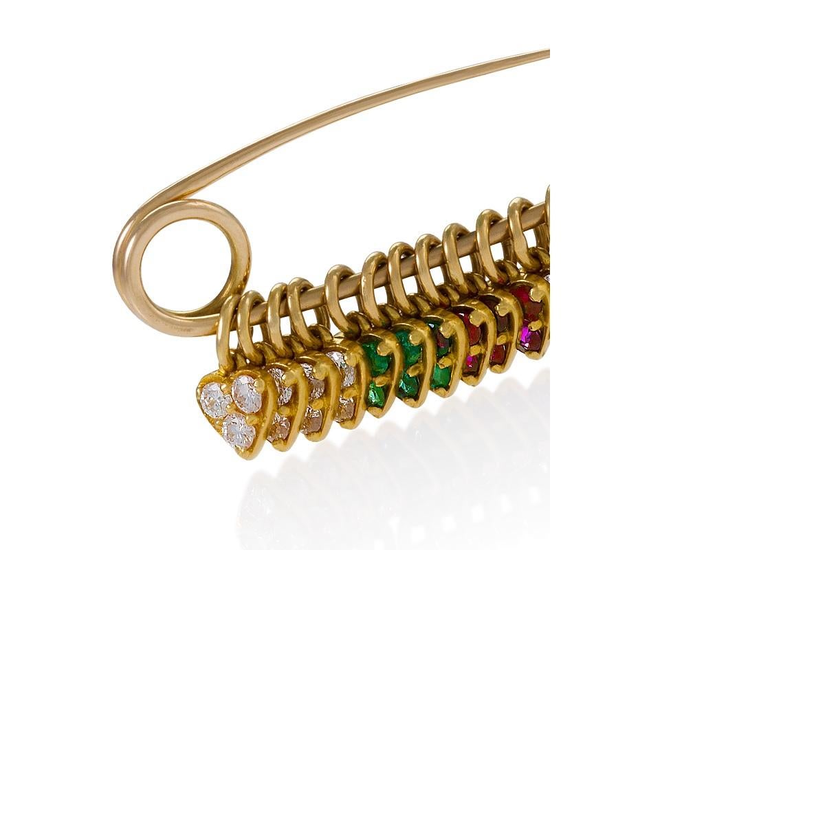 An American modern safety pin brooch in 14 and 18 karat bi-color gold with diamonds, rubies and emeralds. The 14 karat bi-color gold safety pin, suspending fourteen 18 karat gold gem-set and diamond hearts, has 36 round brilliant-cut diamonds, with