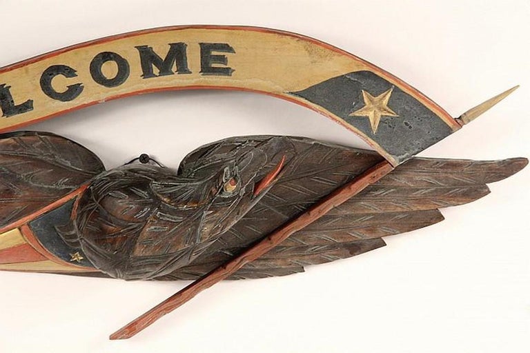 This is a hand-carved American folk eagle in the style of John Bellamy. This particular example includes a hand-painted banner on a staff, which reads 