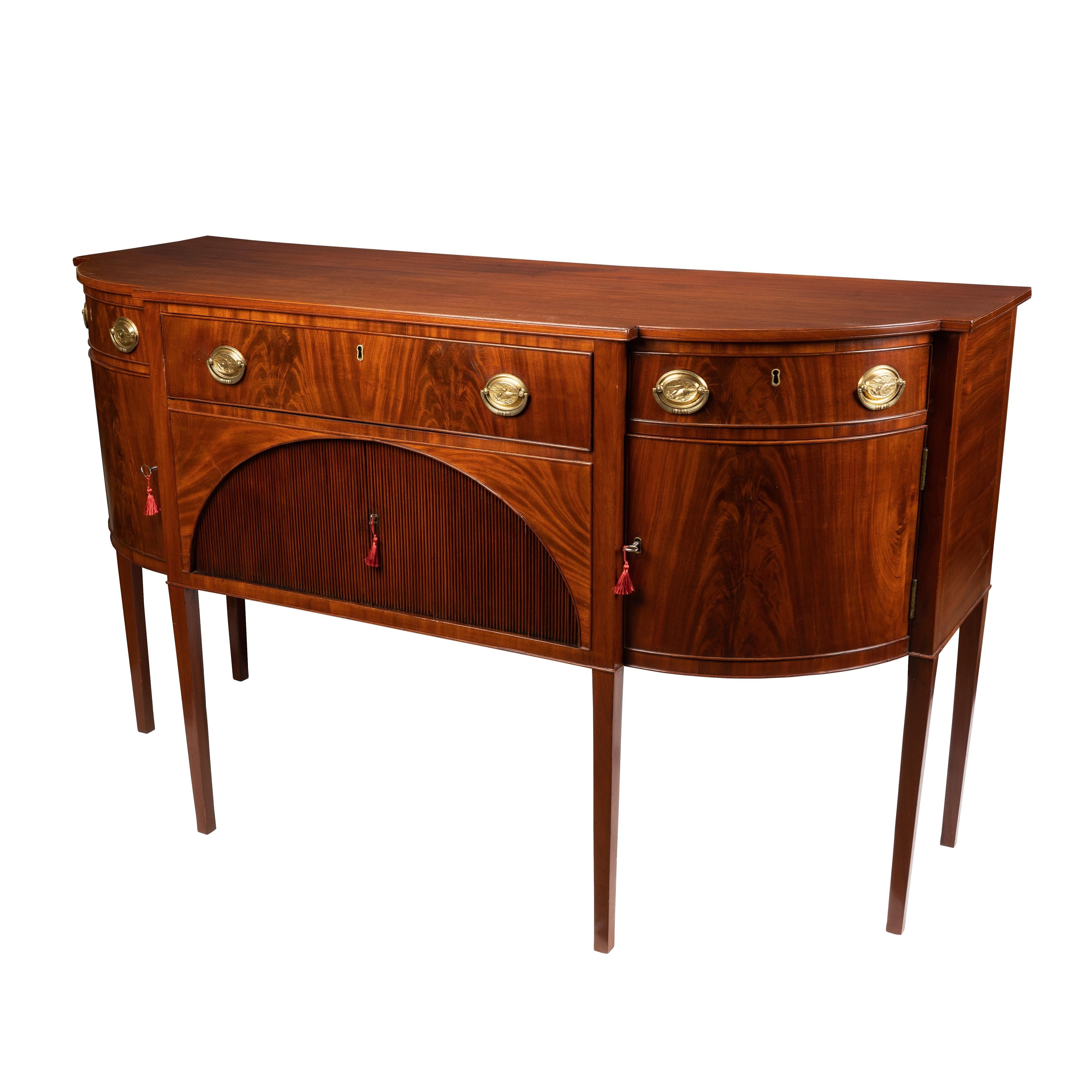 American Hepplewhite side board of mahogany and matched figured mahogany veneers. Northern White Pine secondary wood. The cabinet retains its original stamped brass oval back plates & cast bails. The case is centered on a lunette opening with