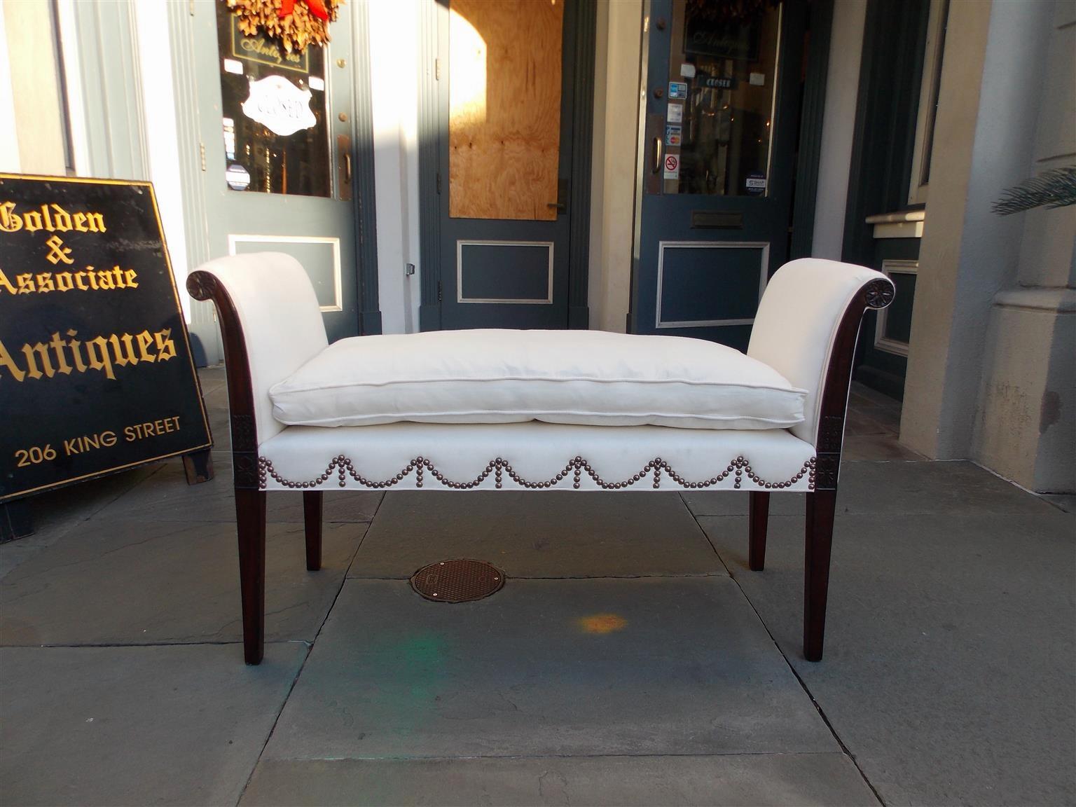 American Hepplewhite mahogany upholstered window bench with flanking scrolled arms, carved rosette medallions, padded cushion, brass swag tacks, and resting on tapered squared legs, Early 19th century. Bench is upholstered in white muslin with