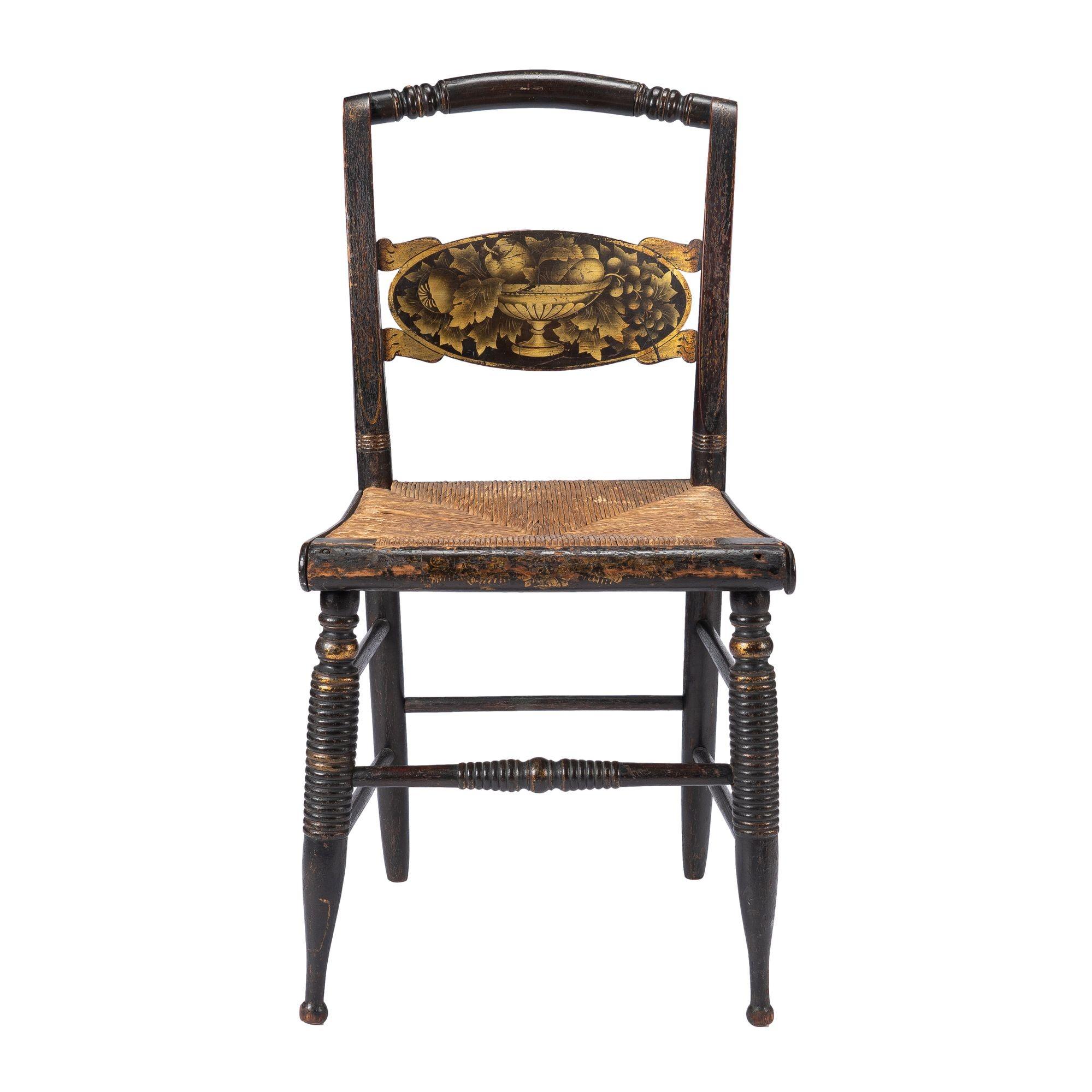 American turtle back, Hitchcock type, rush seat side chair. The back splat features the original gilt and bronze powder stencil decoration of an ornate pedistal base bowl holding fruit and surrounded by leaves. Gilt decorations on the back supports,