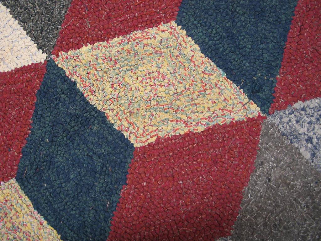 The “tumbling block” design of simultaneously projecting and receding cubes made up of lozenges in red, royal blue, ecru, straw and light blue is a popular pattern on both American quilts and hooked rugs. This reversing trompe l’oeil pattern also