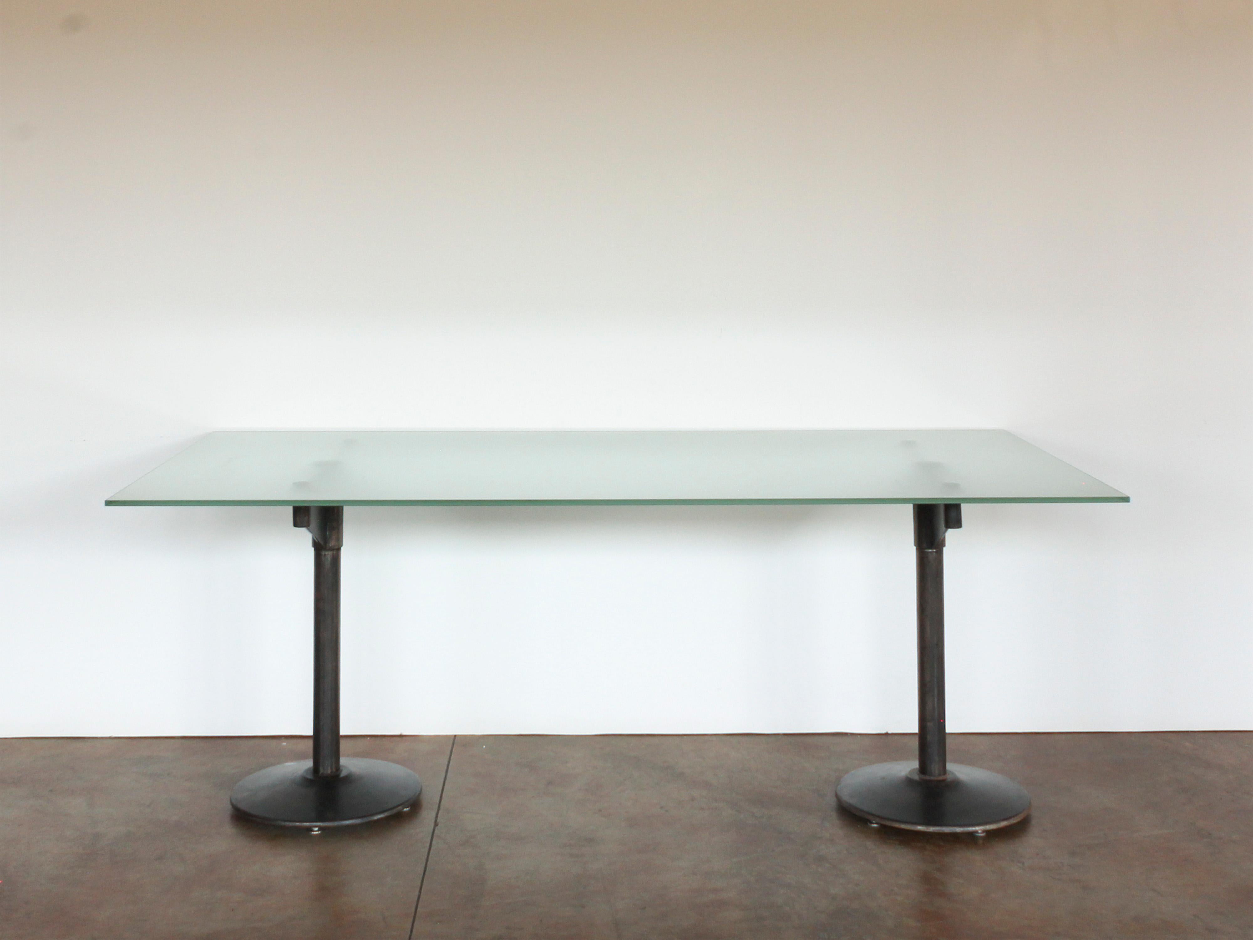 table de style industriel américain du 20e siècle reposant sur deux piédestaux en fer avec plateau en verre dépoli.