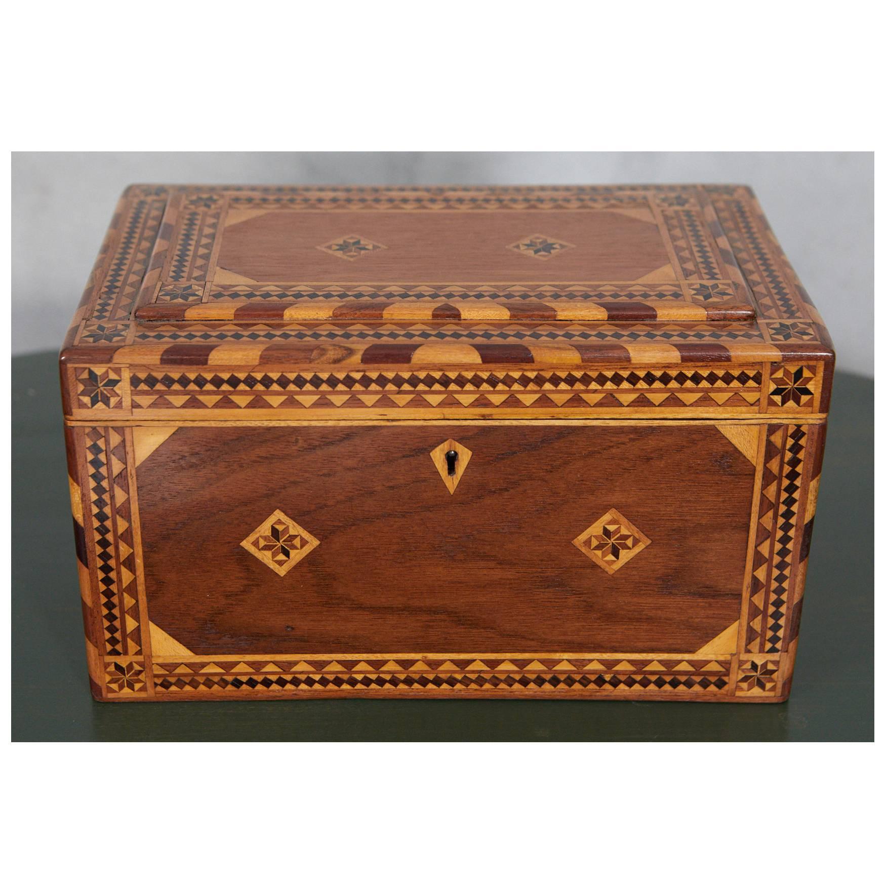 An impressive example of craftsmanship, this box has been inlaid with various woods in decorative designs and patterns with a stepped top detail. The interior has a metallic gold painted rim.
 