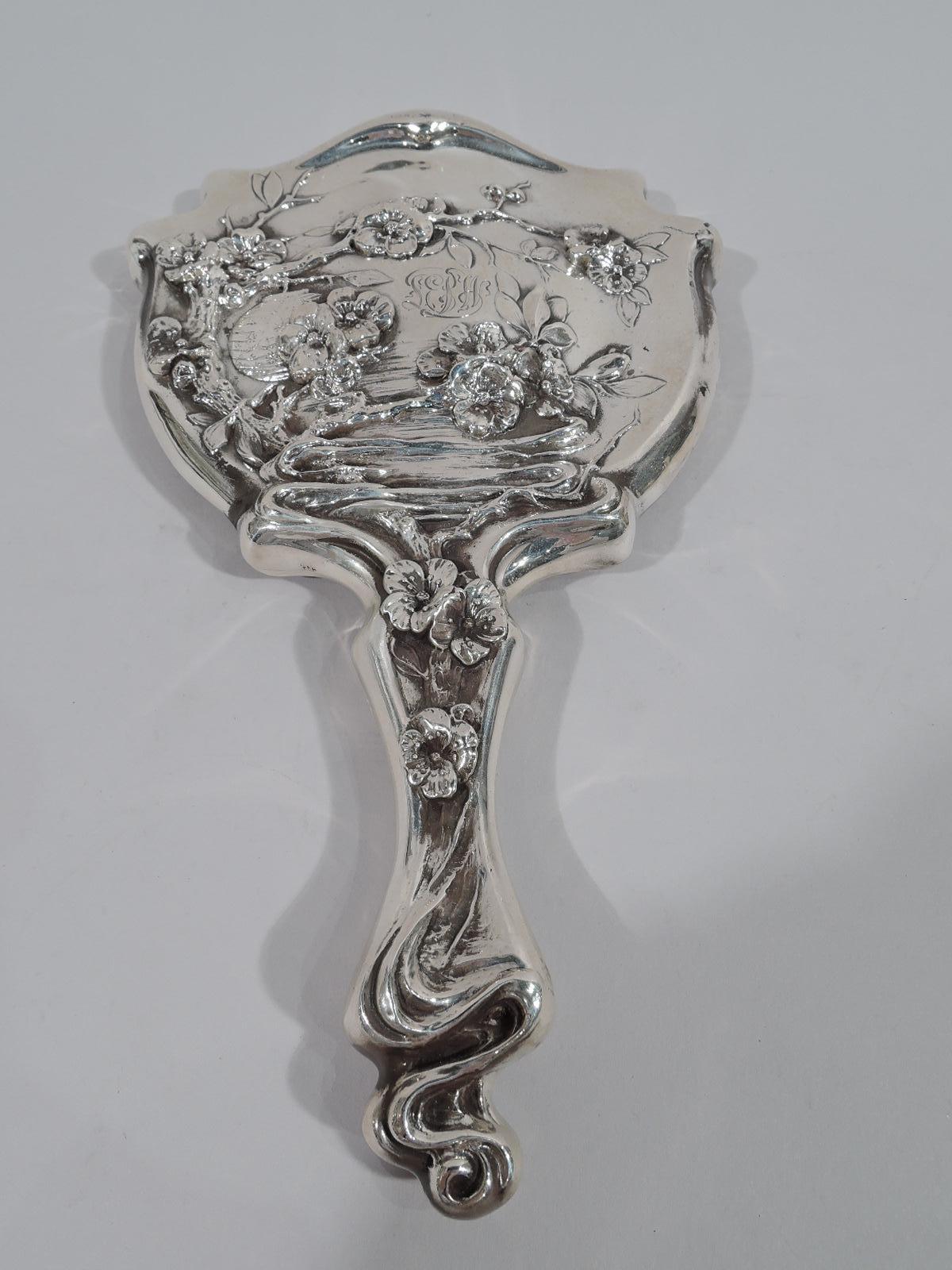 Turn-of-the-century American Japonesque Art Nouveau sterling silver geisha vanity set. This set comprises hand mirror and hair comb. Both are shaped with whiplash curves and blossoming prunus branches. Mirror glass beveled. Mirror back engraved with