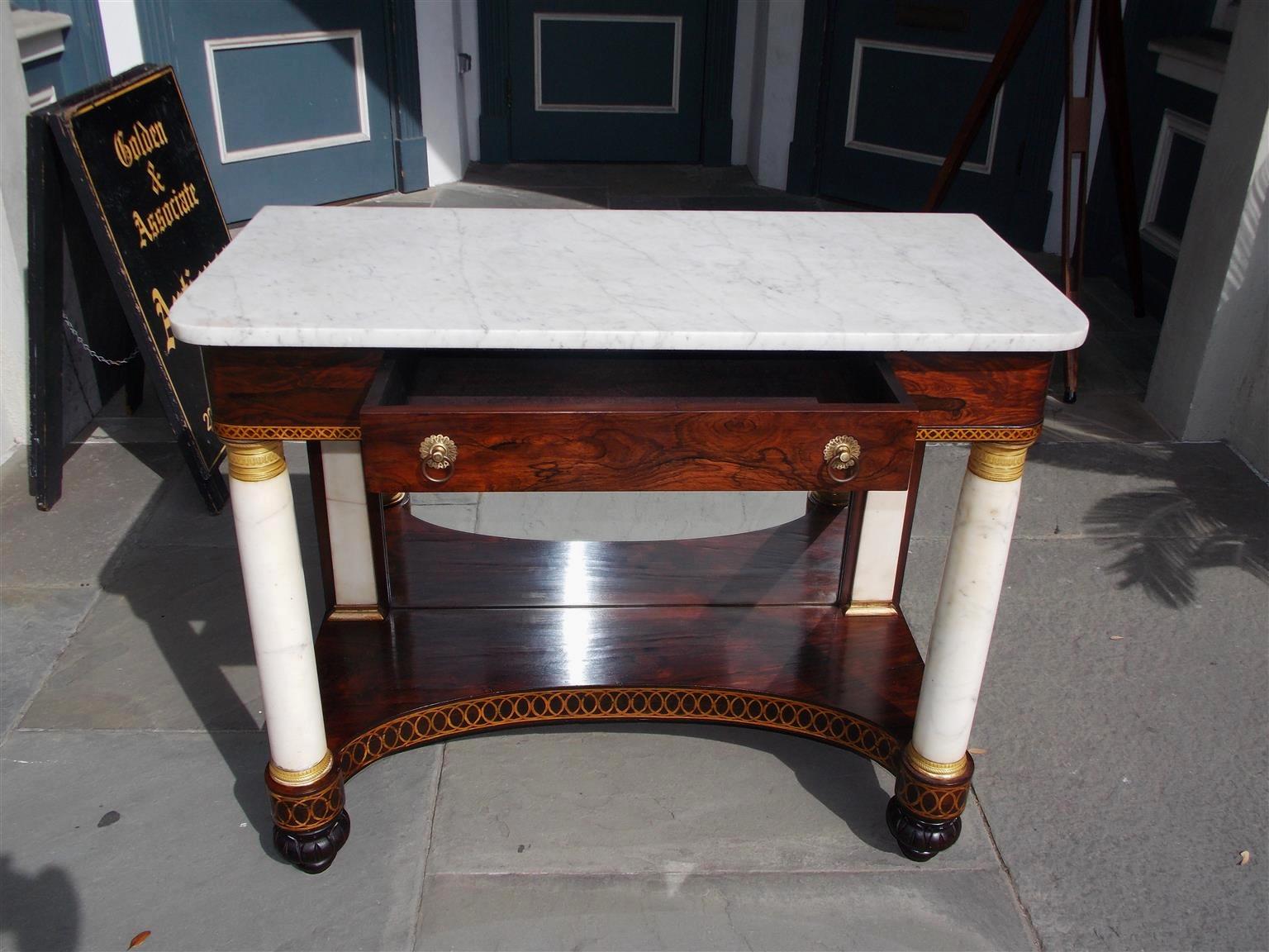 American kings wood marble-top one drawer console with the original brasses, gilt stenciling and ormolu mounts, flanking marble columns, and terminating on the original decorative carved floral melon feet. Console retains the original silvered