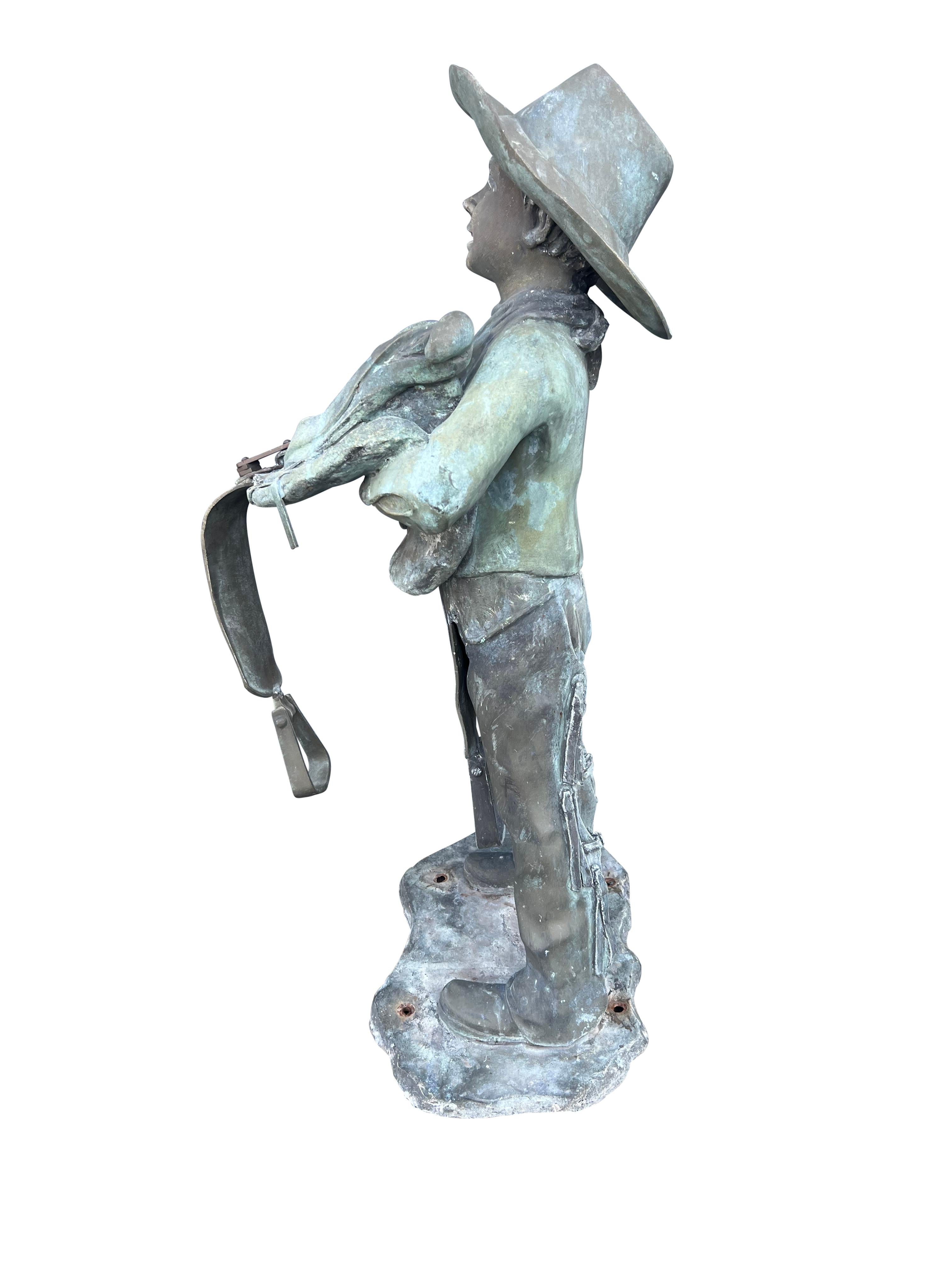 Boy with cowboy hat holding a saddle wearing chaps. This has been outdoors and has a verdigris patina.