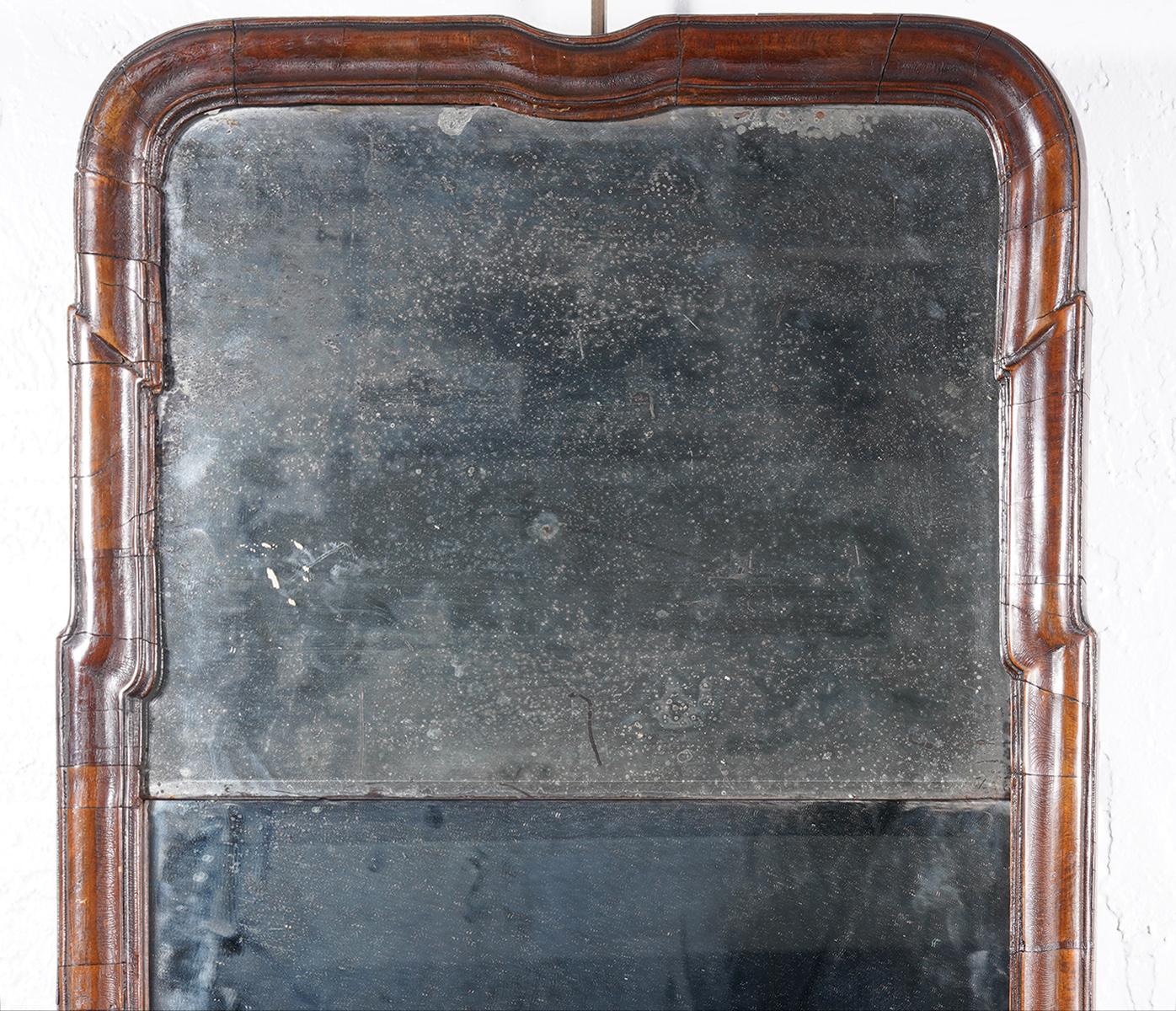 This American Queen Anne style mirror dates to the mid-1700s and features a sectioned cornice profile walnut frame and a two part mirror. The upper mirror is original, the lower later. The top is shaped in a typical and subtle Queen Anne tradition