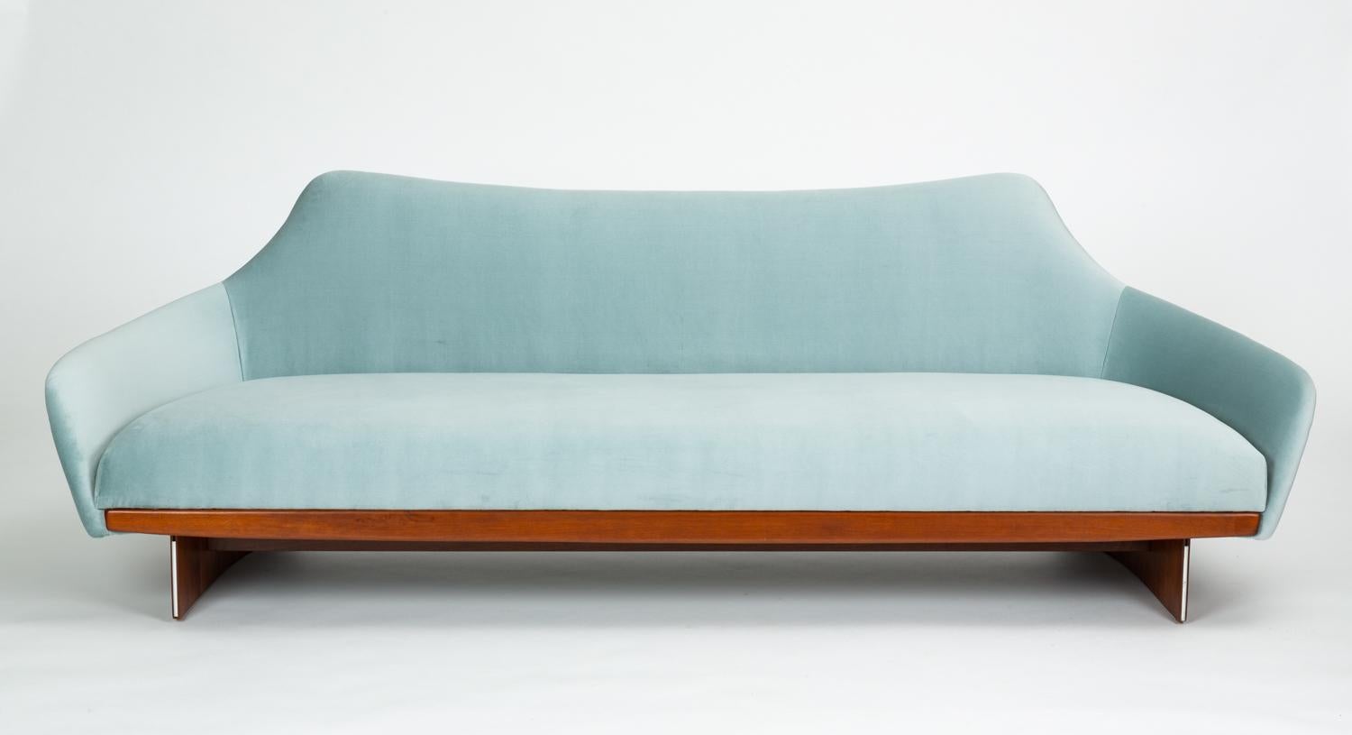 A unique design in the style of Adrian Pearsall’s angular modernism, this gondola-style sofa has a broad seat with integrated cushions in ice blue velvet upholstery. The peaked backrest is framed on either side with a curved panel of walnut veneer