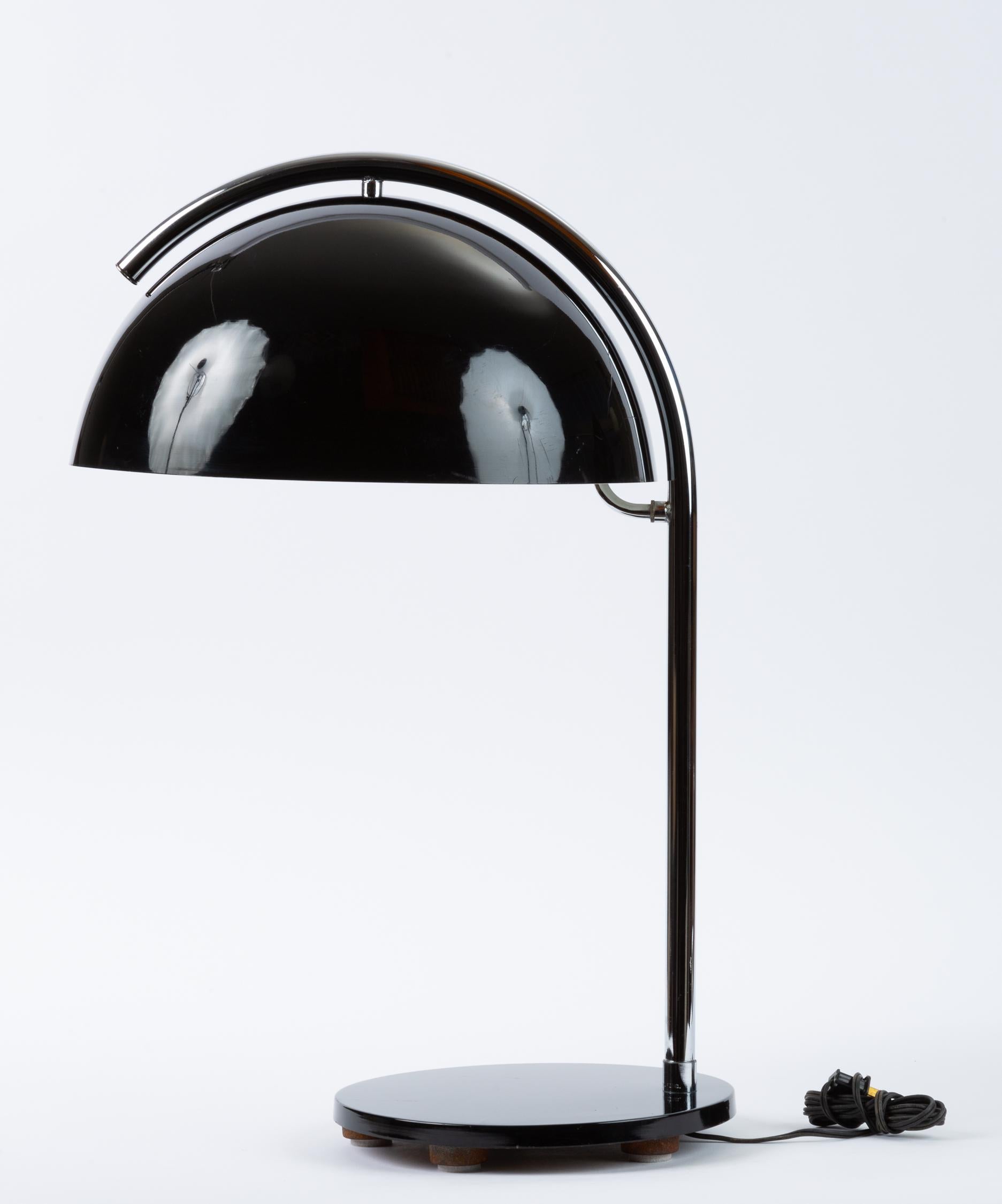 A tall table lamp with an arcing steel arm and a generous mushroom lampshade in black-enameled metal. A round base in matching black anchors the lamp, concealing a stabilizing weighted iron foot. A curved steel branch reaches from the arm beneath