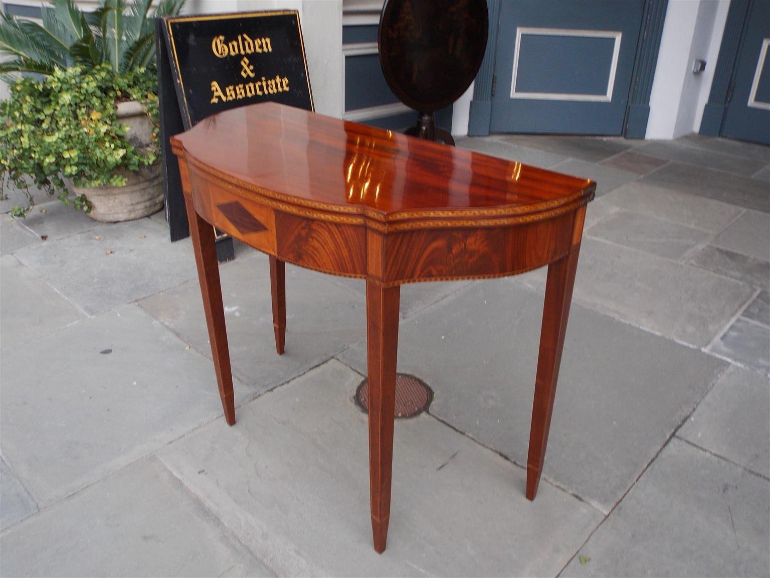 American mahogany half-serpentine form and elliptic front hinged card table with a centered mahogany diamond surrounded by birch inlays, flanking book matched crotch mahogany's, corner rectangular birch inlaid blocks, tulip wood inlaid checkering,