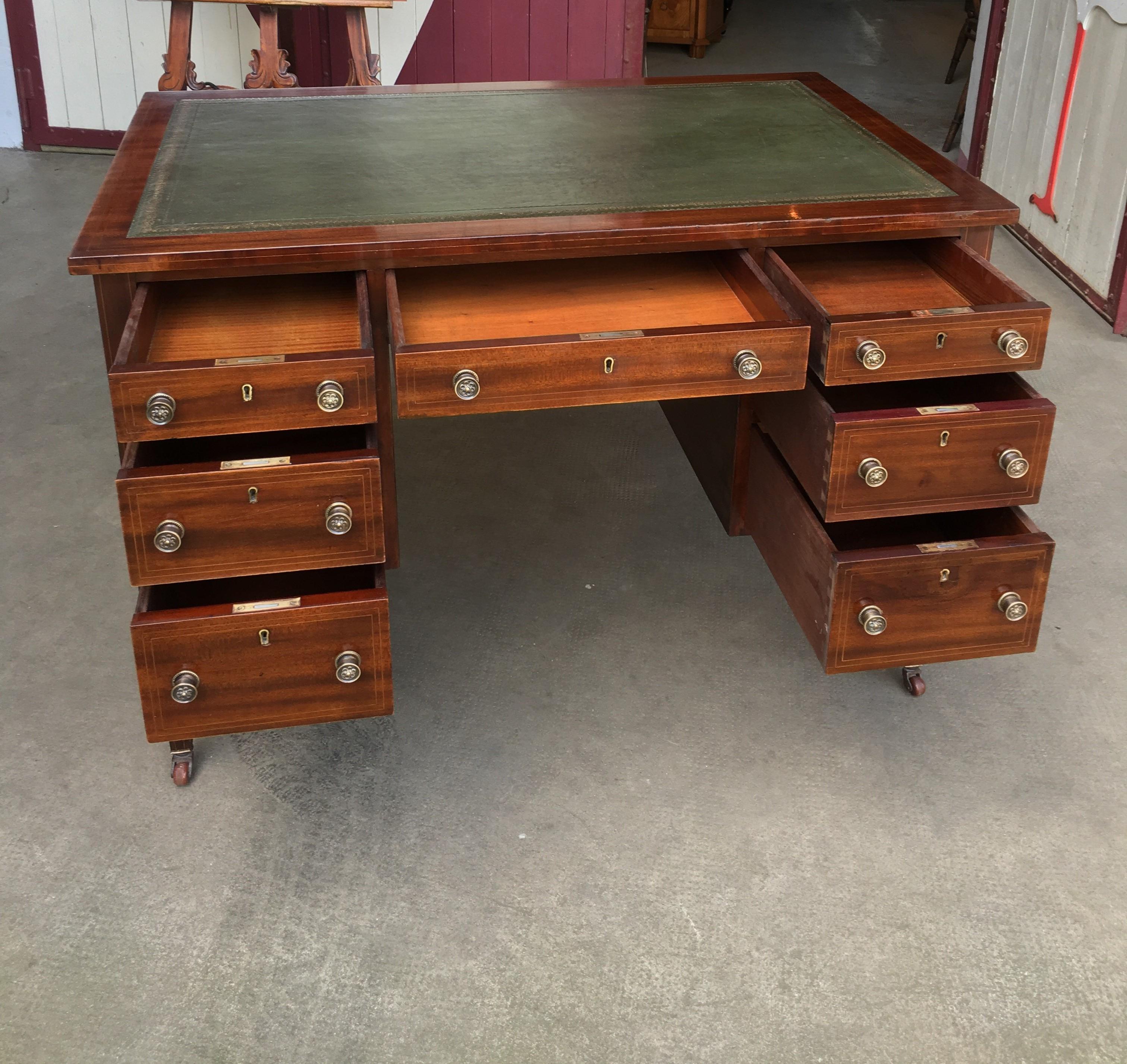 This is a mahogany desk from circa 1914. The writing area is equipped with a leather pad and a gold edge. Seven drawers offer a lot of storage space into the piece. Original brass emblem and buttons are located on the front and back. The whole piece