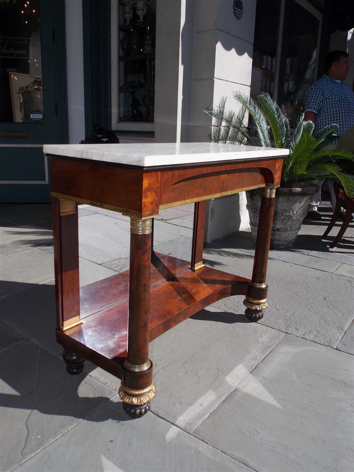 American mahogany marble top console with gilt stenciling skirt, flanking ormolu mounted mahogany columns, and terminating on the original gilt carved floral melon bulbous feet. Console retains the original marble, silvered mirror, and wood backing,