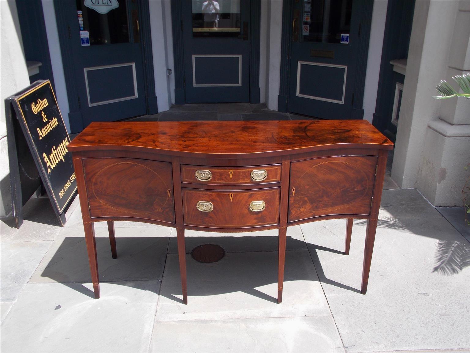 American mahogany serpentine brandy board with two graduated centered drawers, diamond satinwood inlaid escutcheons flanked by period rectangular eagle brasses, two hinged cabinets with flanking oval satinwood inlays, and terminating on the original