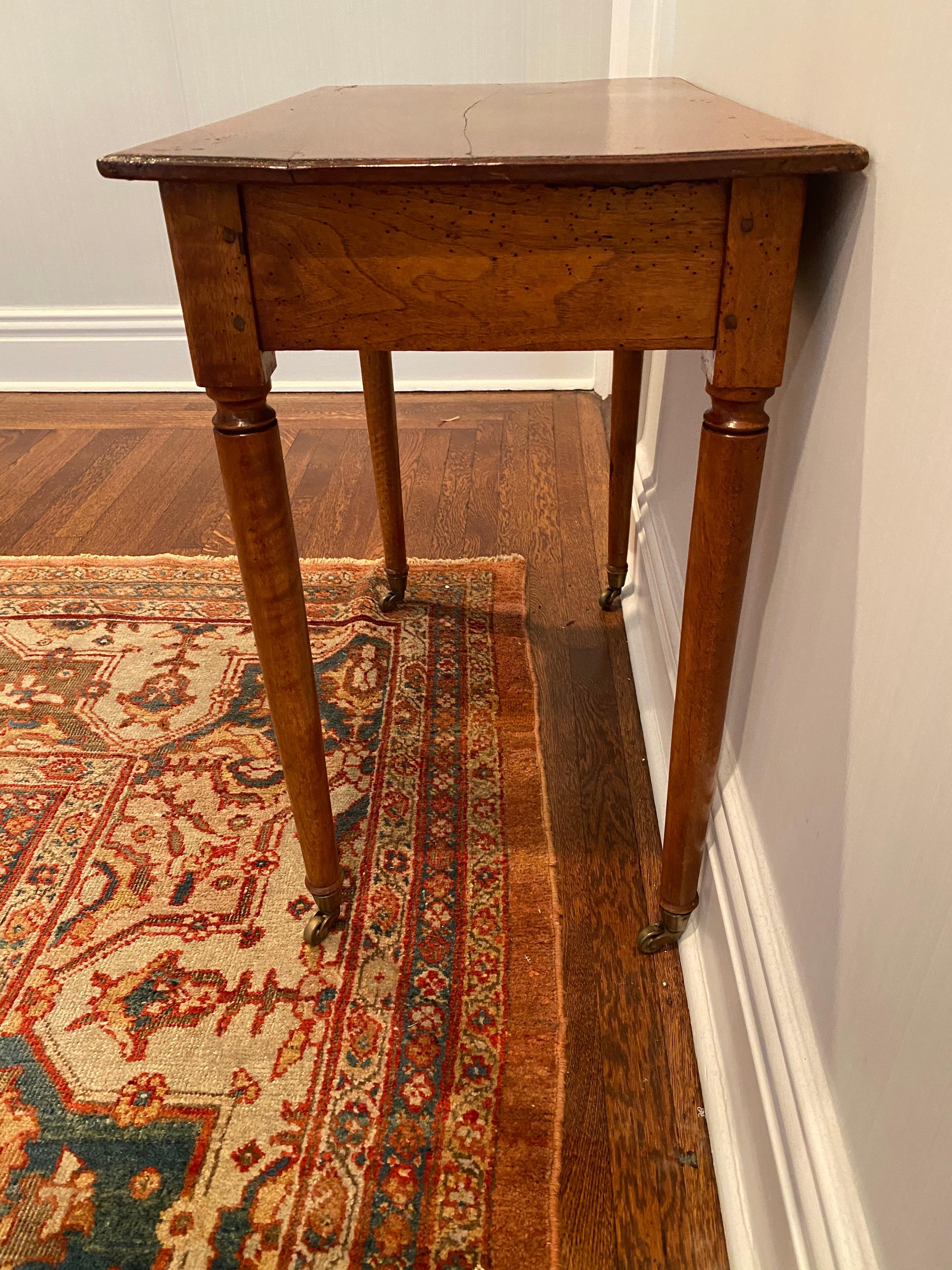 American mahogany single drawer side table
Rounded tapered legs on casters. 
Split to wood on top, in good stabile condition. 

Measures: 30” W x 17.5” D x 28” H 
Drawer 13” D x 23” x 2” D 
Floor clearing 23.5”.