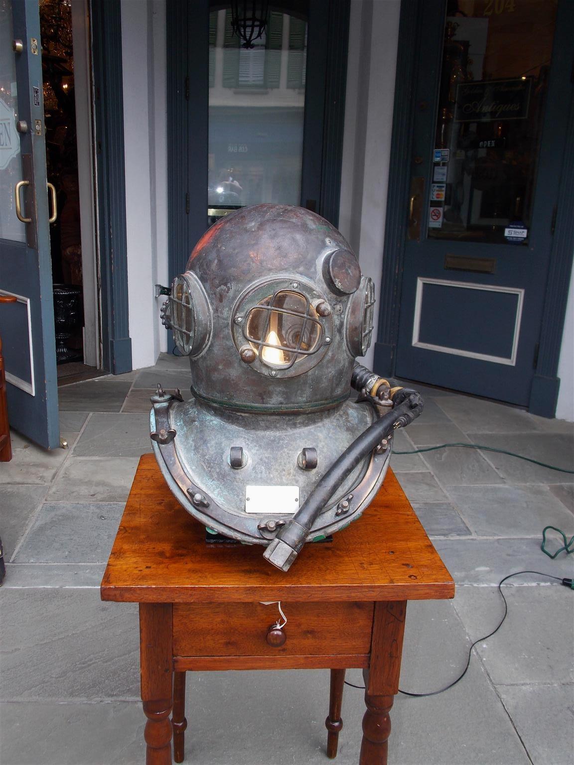 American maritime copper and brass deep sea divers helmet with the original three glass cross hatched windows, latching bonnet, air line intake with hose, and exterior mounted rear ventilator, Early 20th century. Helmet has been electrified on a