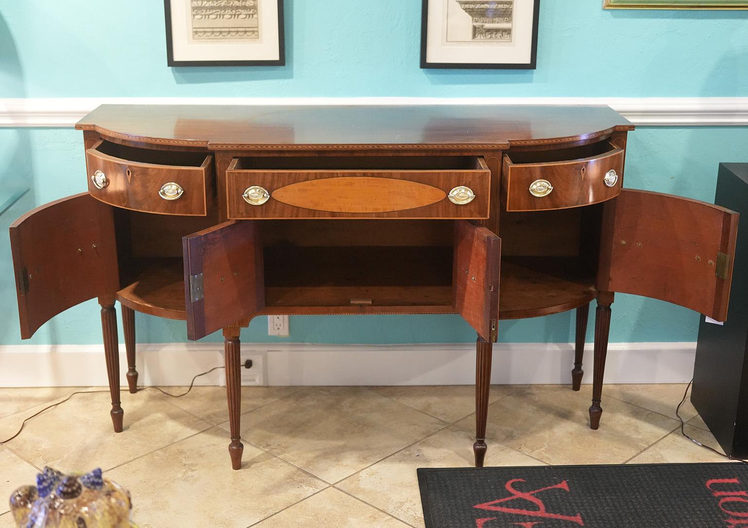 Beautifully inlaid mahogany Sheraton North Shore, Massachusetts American sideboard. Three drawers over four doors resting on turned and fluted legs. Central drawer has satinwood inlaid oval panel. Circa 1820s. 