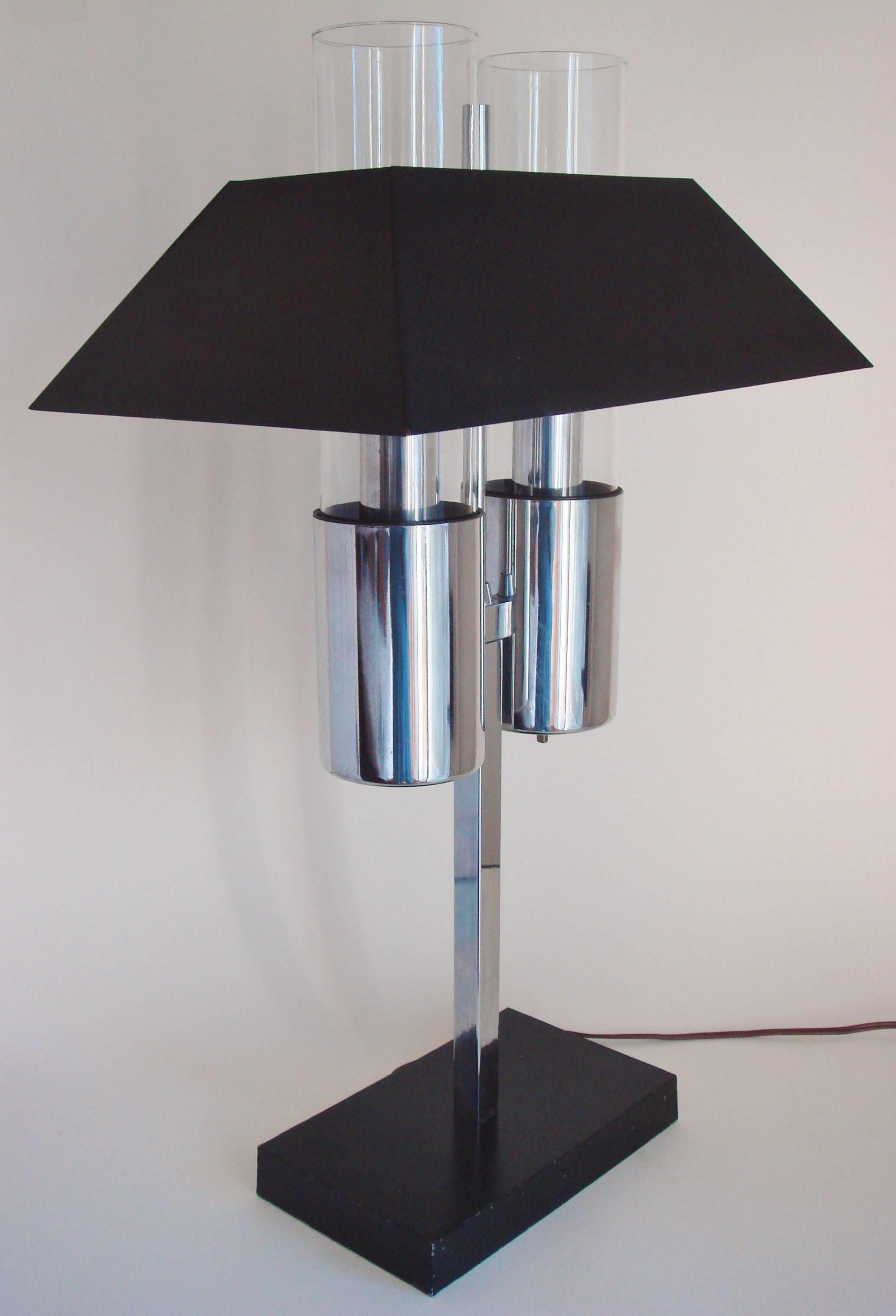 This stunning large American Mid-Century Modern twin bulb banker's lamp features a chrome body with a black enameled shade and base with twin glass chimneys for each black plastic lined bulb socket. This lamp was a product of the company Raymor who