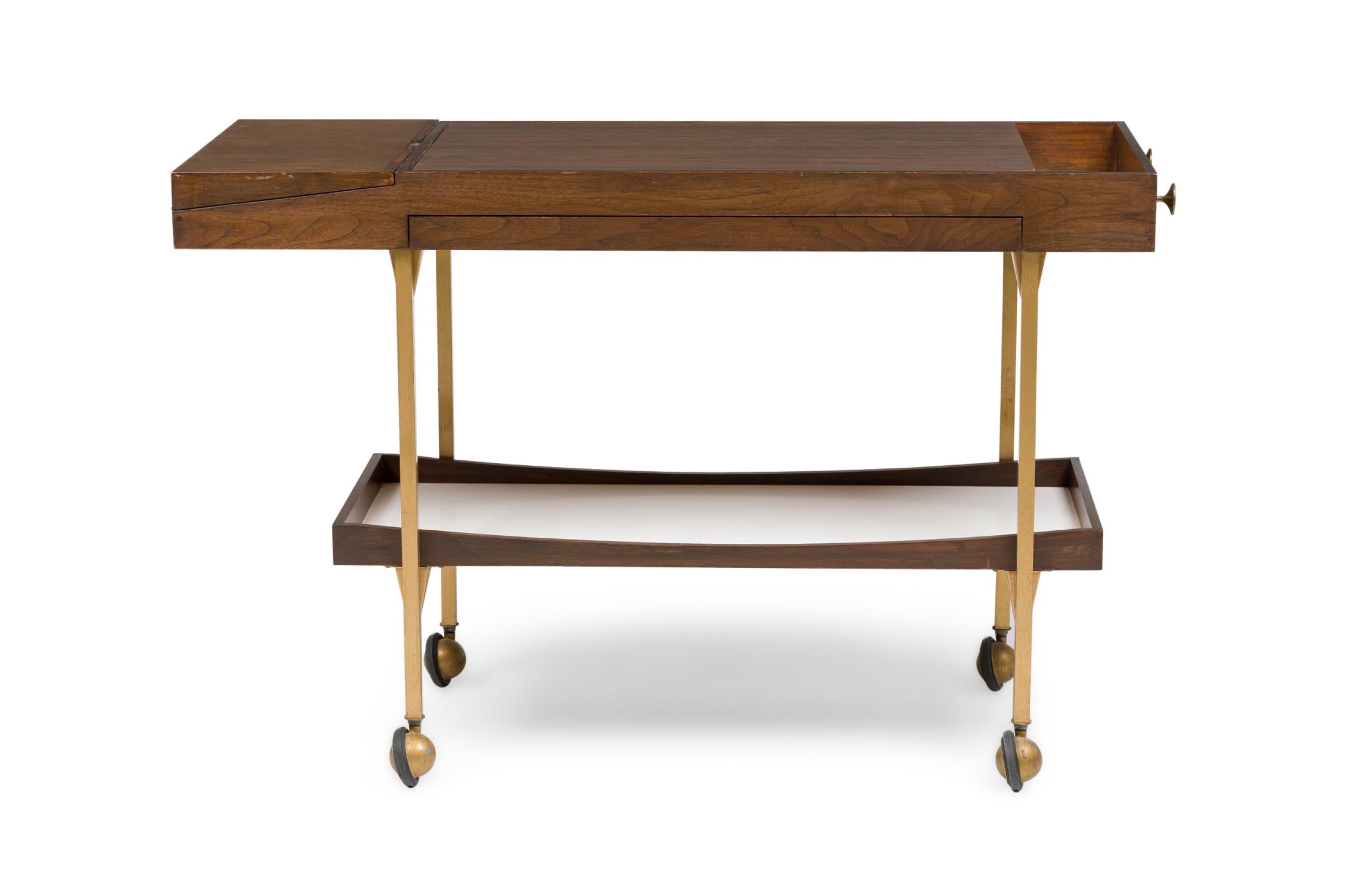 American Mid-Century wood bar cart featuring a lower shelf and a top having a hinged fold out small draw and a pull out top shelf supported on 4 round brass legs (Milo Baughman)
