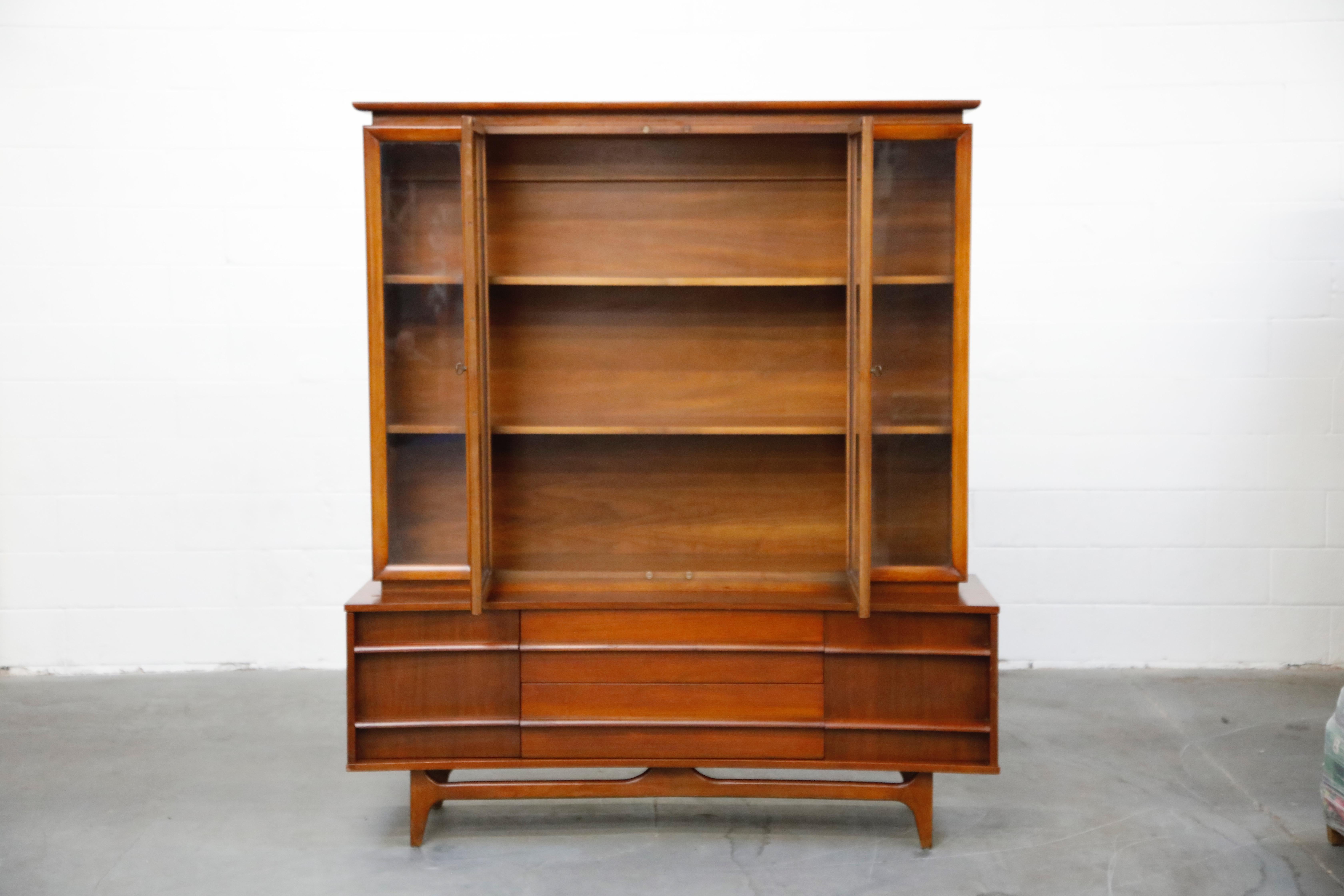 This large American Modern sideboard credenza and hutch wall unit has beautiful midcentury details adorning its exterior and ample storage inside. The top china cabinet has four glass windows, two of which are doors that open into the shelving