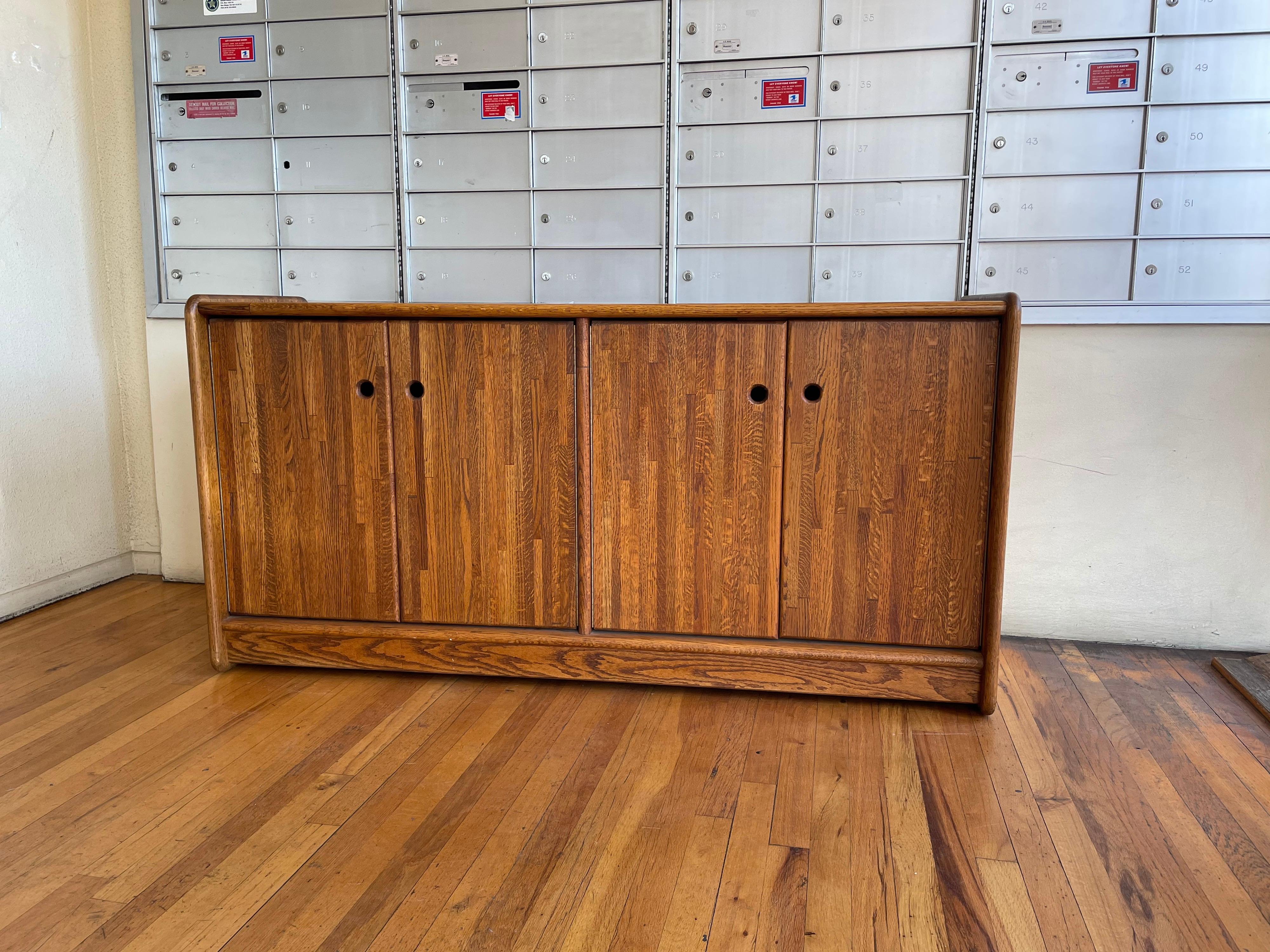 Beautiful simple and well constructed solid oak double door credenza, circa 1980's we believe it was designed by Lou Hodges, great original condition very clean we have oiled the piece, has a walnut stain finish. With shelf and drawer on one side