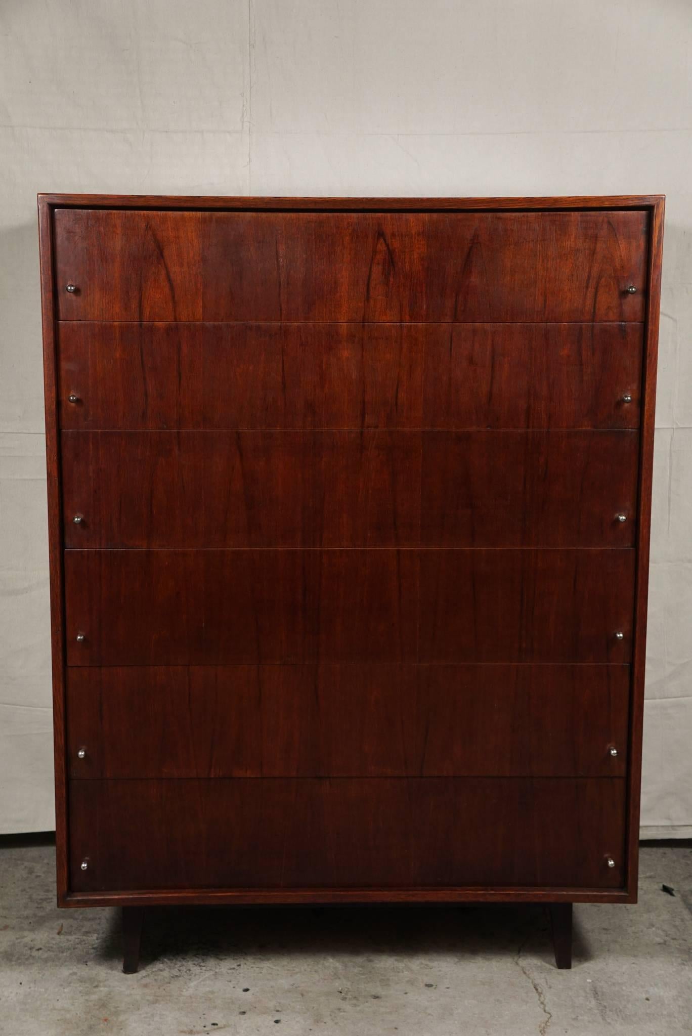 This beautiful and simple tall chest housing six large drawers was made in America in the late 1950s. Constructed of a dark rich walnut veneer chosen to highlight the long grains and growth patterns of the wood down the entire length of the chests