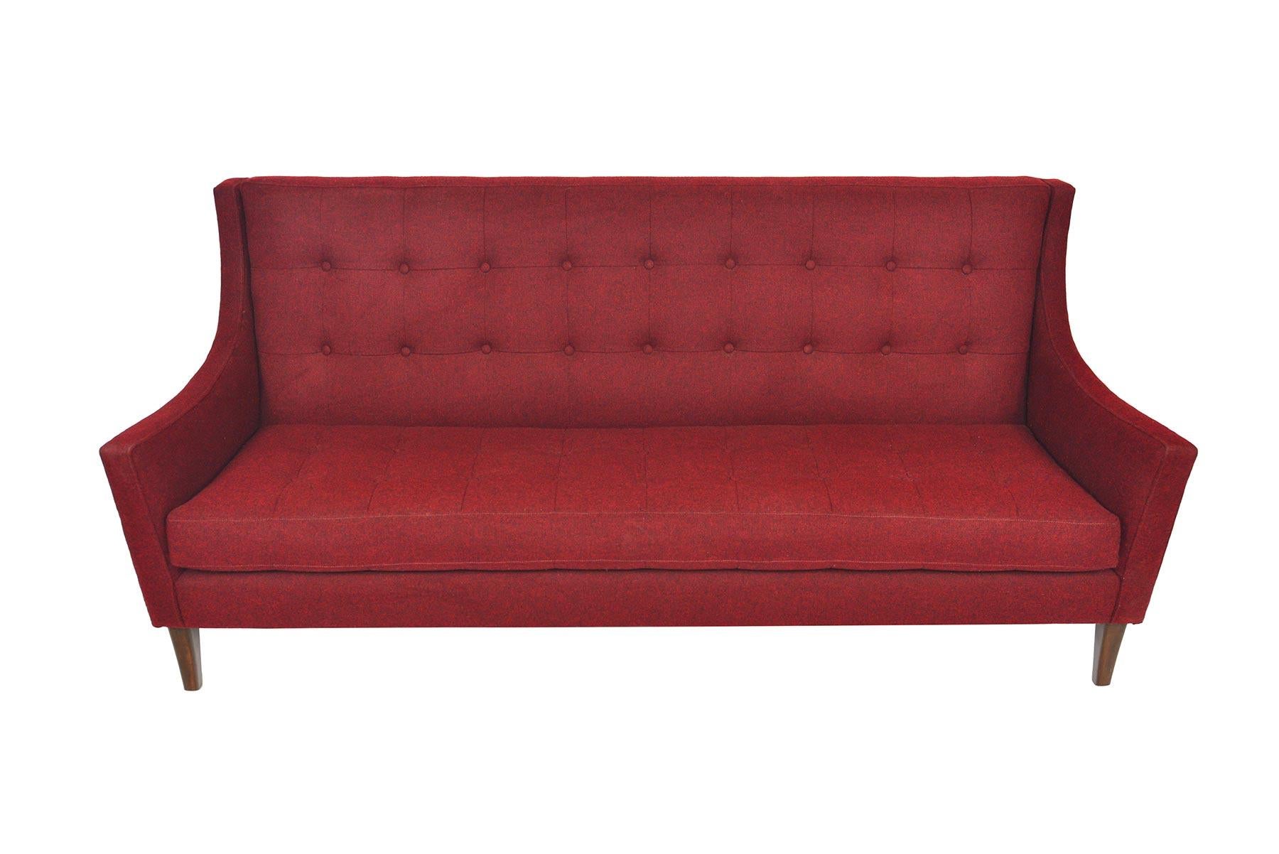 This Classic American midcentury three-seat sofa from the 1950s was designed with a stunning profile! Flared armrests adjoin to the high backrest. Beautifully tufted detailing is featured on the backrest and the removable single cushion. Sofa stands