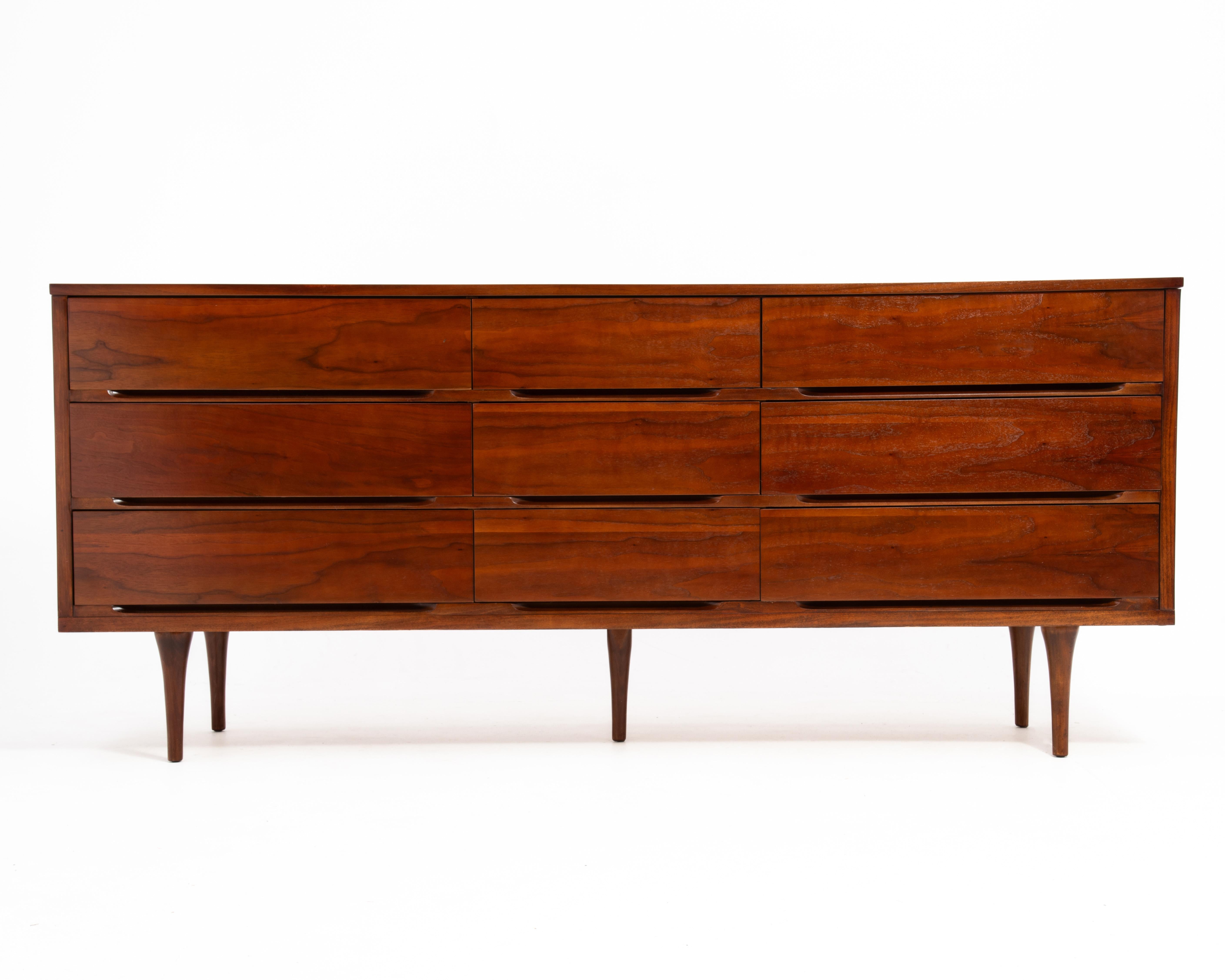A professionally refinished and well kept nine drawer Mid Century American Modern walnut dresser. The walnut is beautiful, well chosen and book matched. This dresser has tapered legs and 9 drawers. The drawers have hidden pulls beneath the drawer