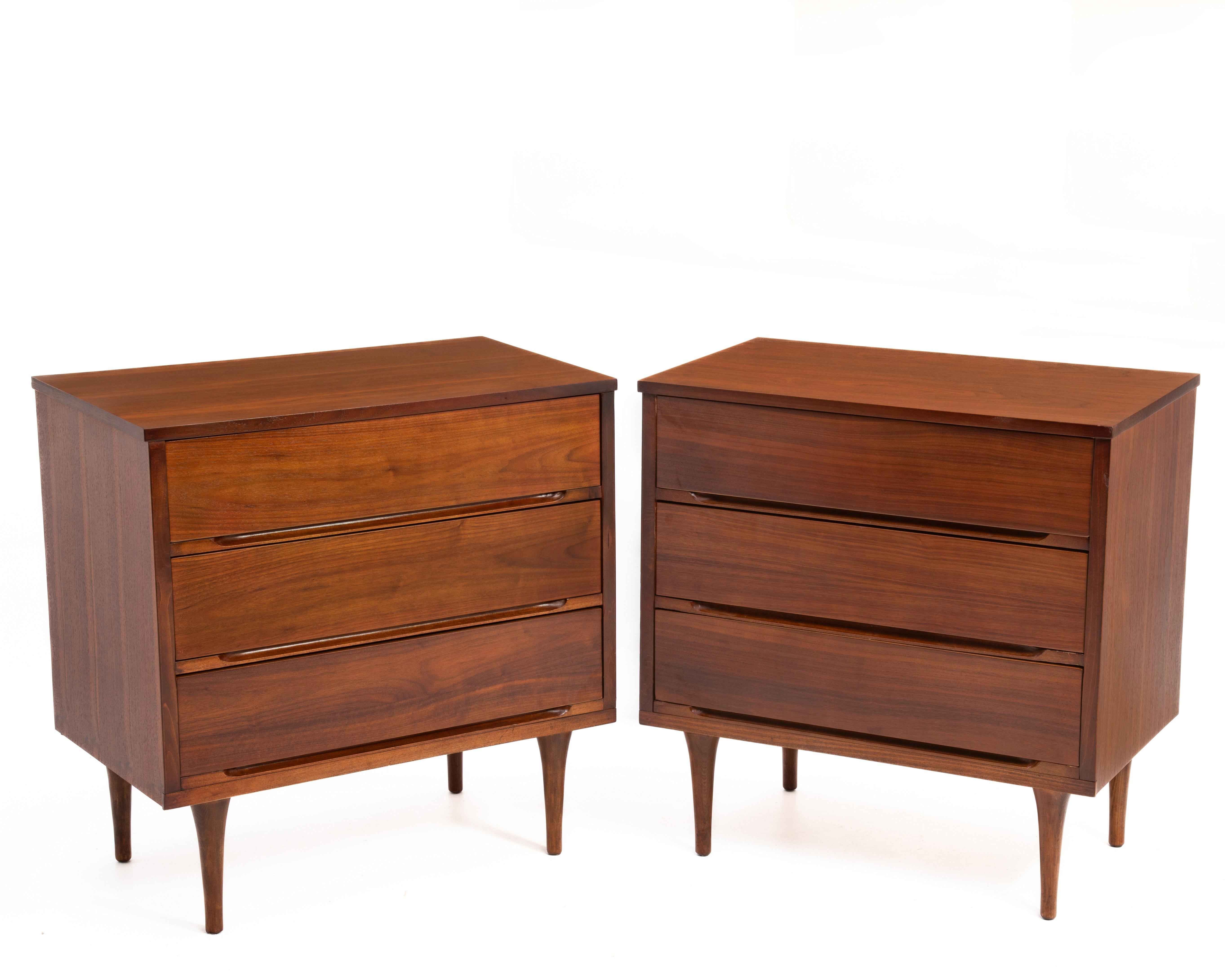 A professionally refinished and well kept pair of Mid Century American Modern walnut three drawer chests. The walnut is beautiful, well chosen and book matched. This chests have tapered legs and each have 3 drawers. The drawers have hidden pulls