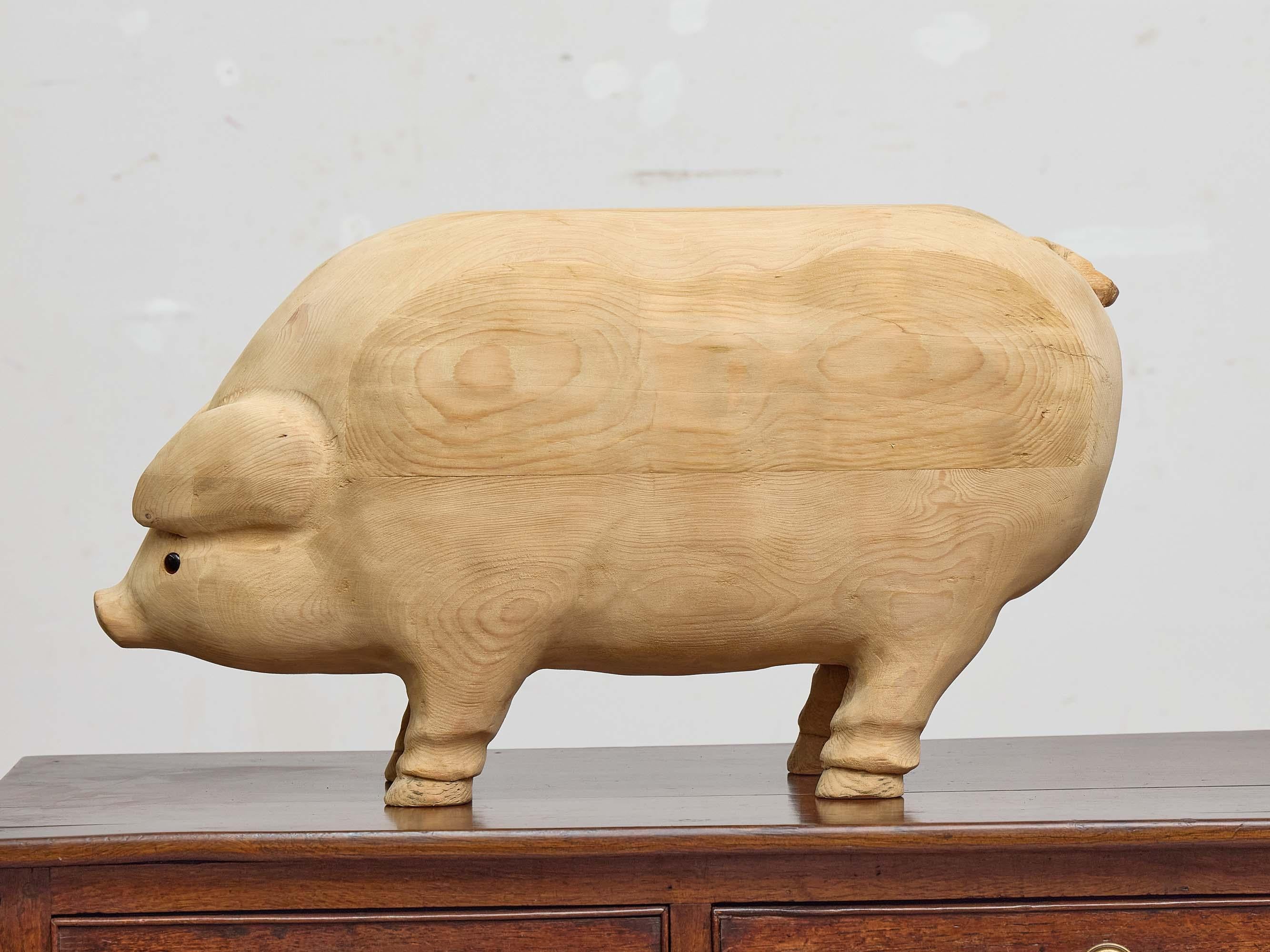 An American Midcentury carved pine pig sculpture, notable for its warm, natural finish and endearing folk-art style. Measuring 22 inches in length, this solid pine figure is hand-shaped with smooth, rounded contours that emphasize the pig’s plump