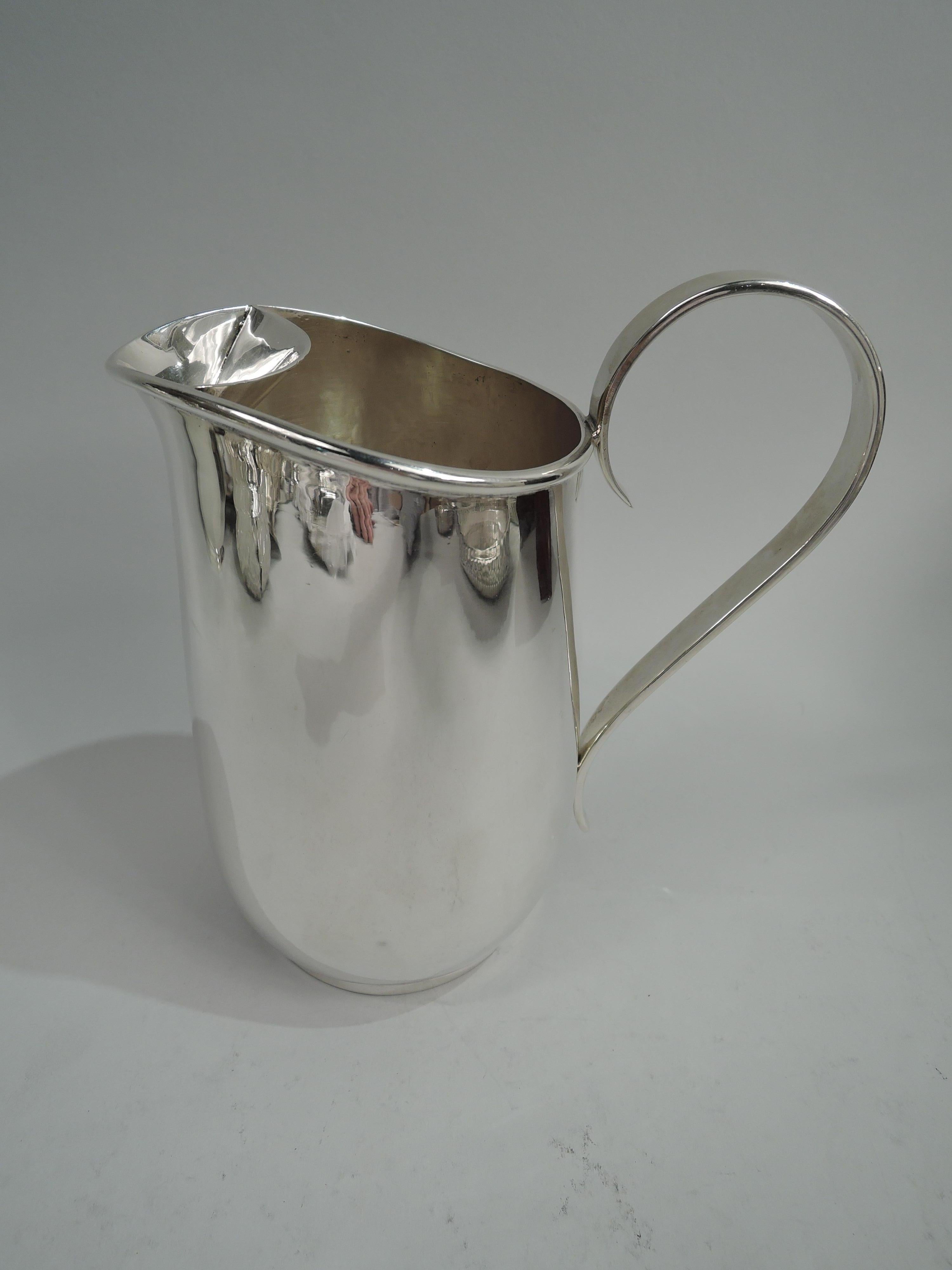 American Mid-Century Modern sterling silver bar pitcher. Round with gently curved sides, short and inset foot ring, and high looping handle. Mouth has lip spout and ice guard. Stylish barware with visible handwork on interior. Perfect for your own