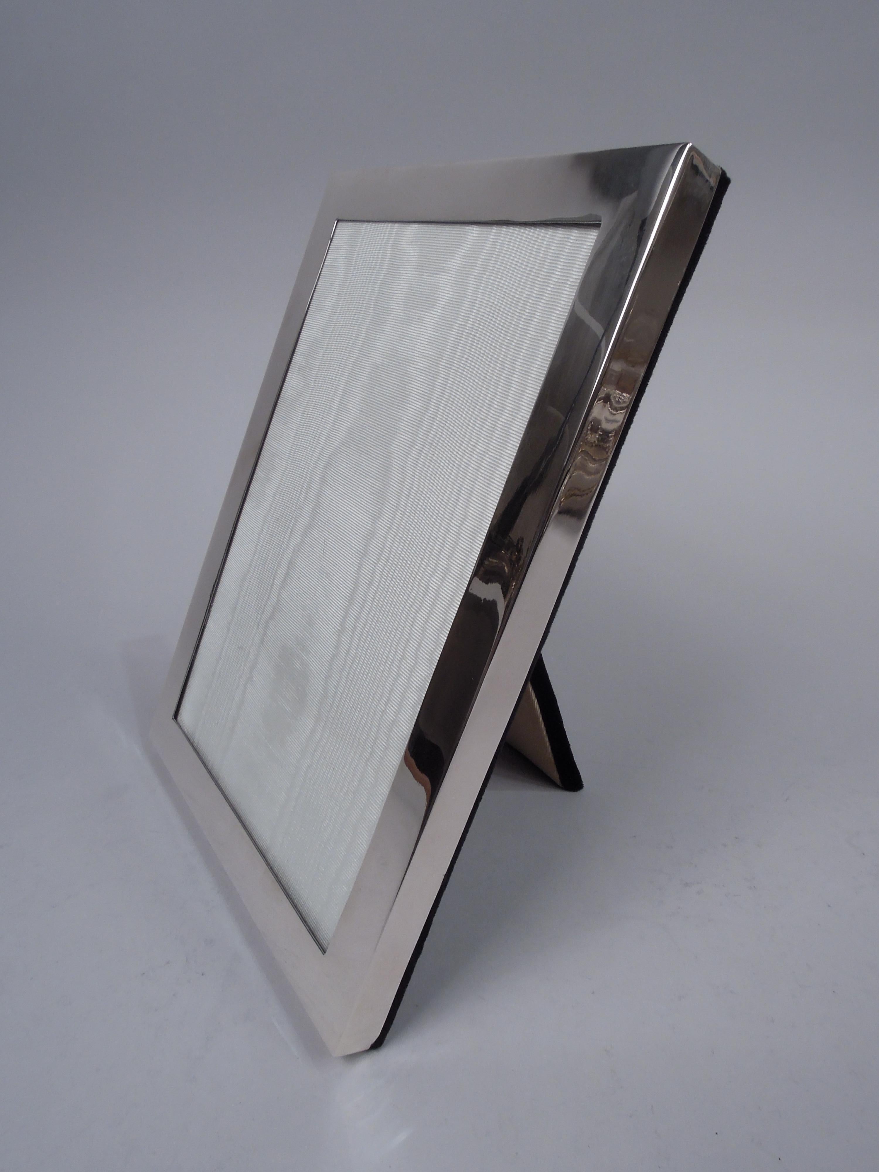 Midcentury Modern sterling silver picture frame. Made by Watrous Mfg. Co. (part of International) in Wallingford, Conn. Rectangular window in clean and unadorned flat surround. With glass, silk lining, and velvet back and hinged easel support for
