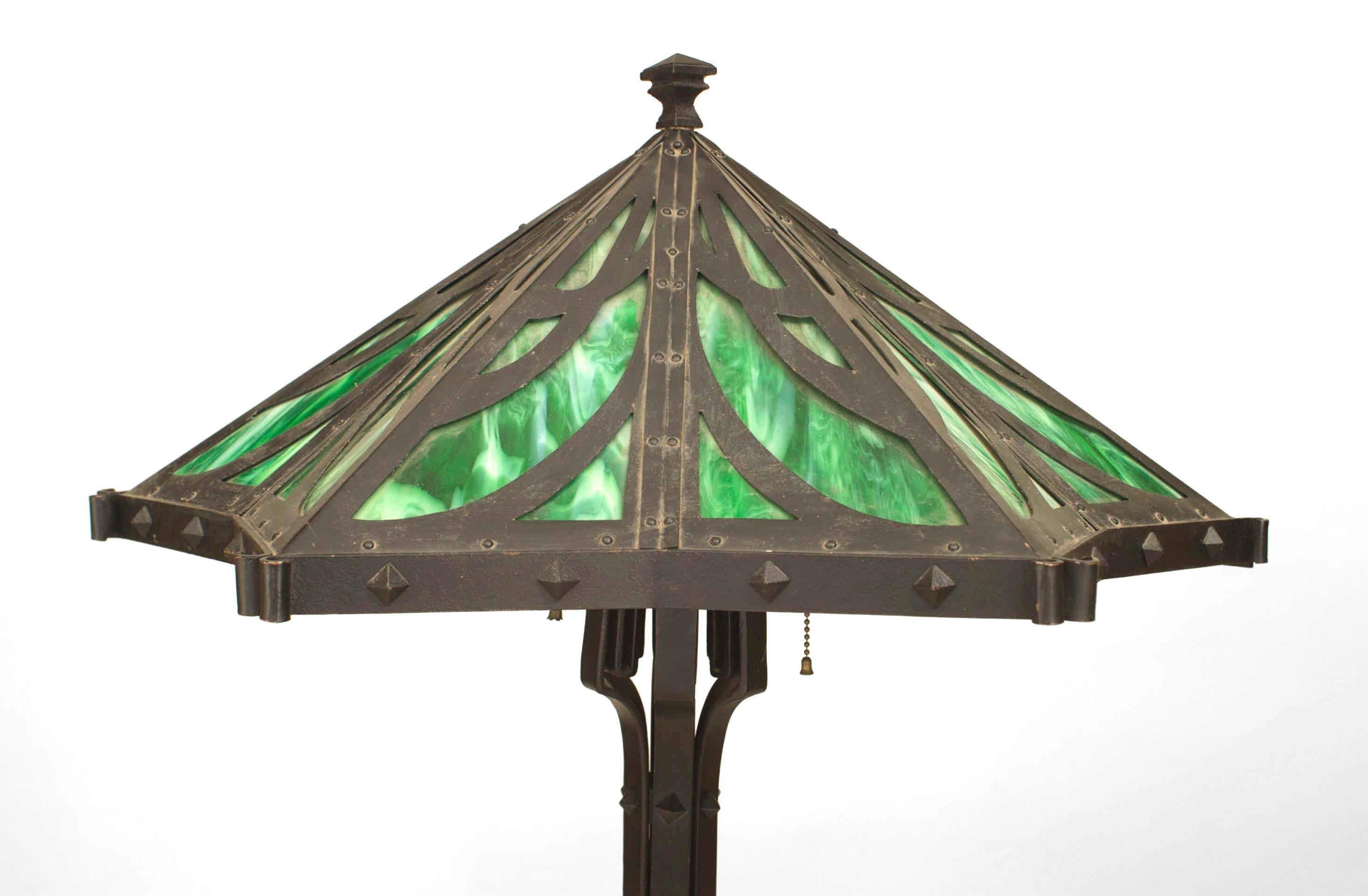 American Mission black iron table lamp having a 6 sided shade with green slag glass cut out design supported on 6 scrolls and trimmed with metal studs.
