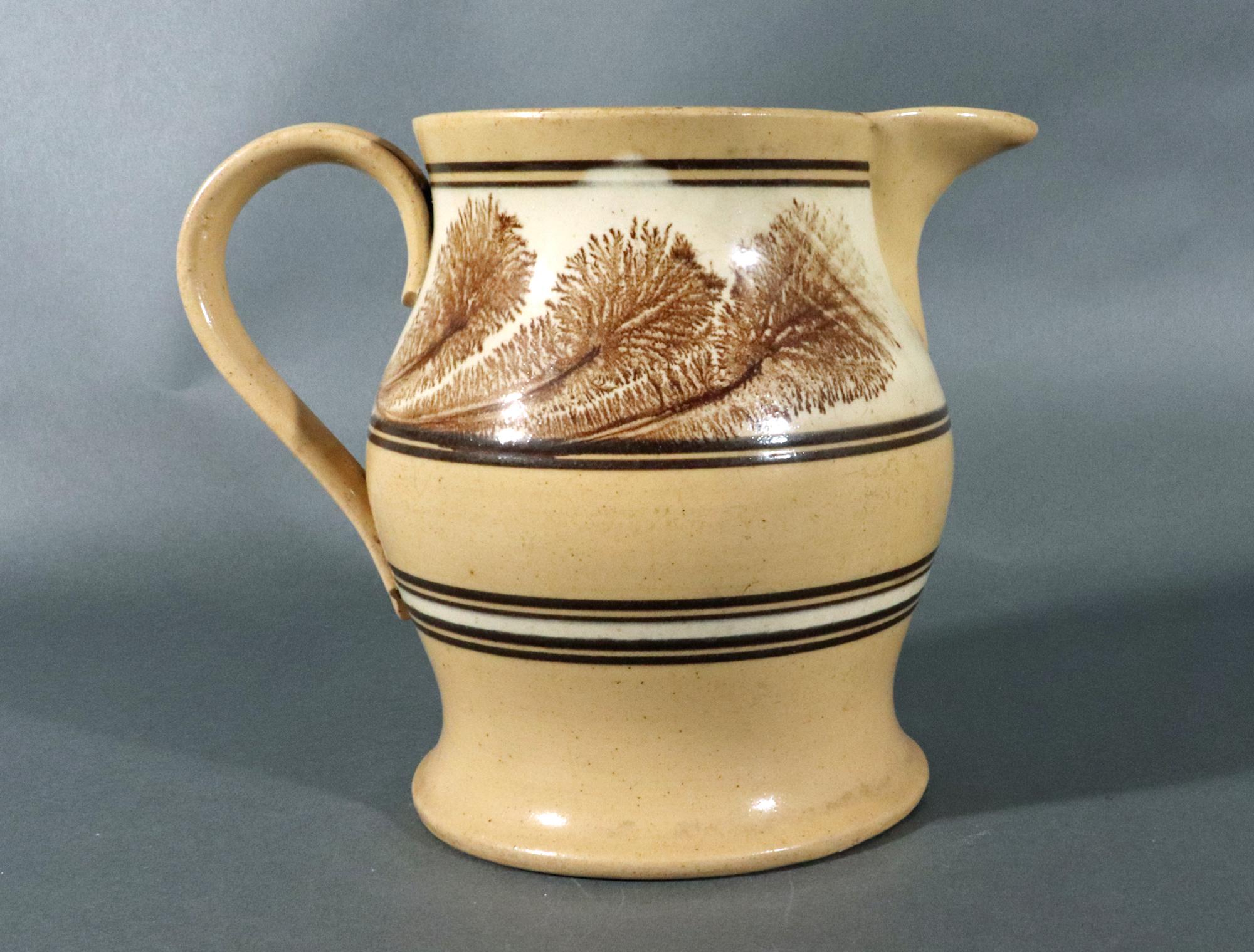 American Mocha Yellow Ware Jug with Puce Seaweed Decoration,
mid-19th century

The American yellow ware bulbous jug has continuous bands of brown and white and a large band of puce sea weed design which runs below the spout and through the ridged