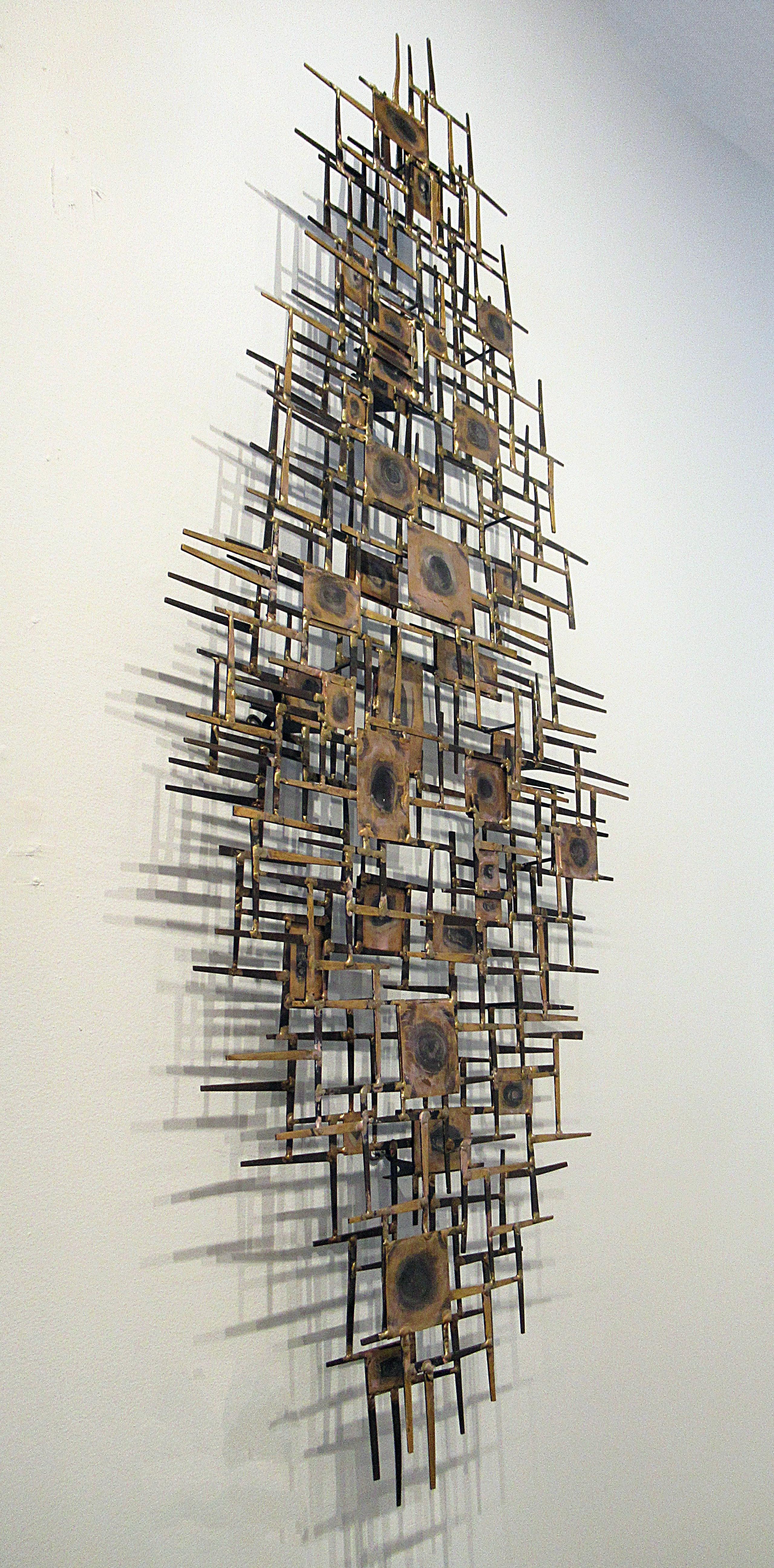 Modern metal wall sculpture features a mix of iron nails, sheet metal and brass accents.