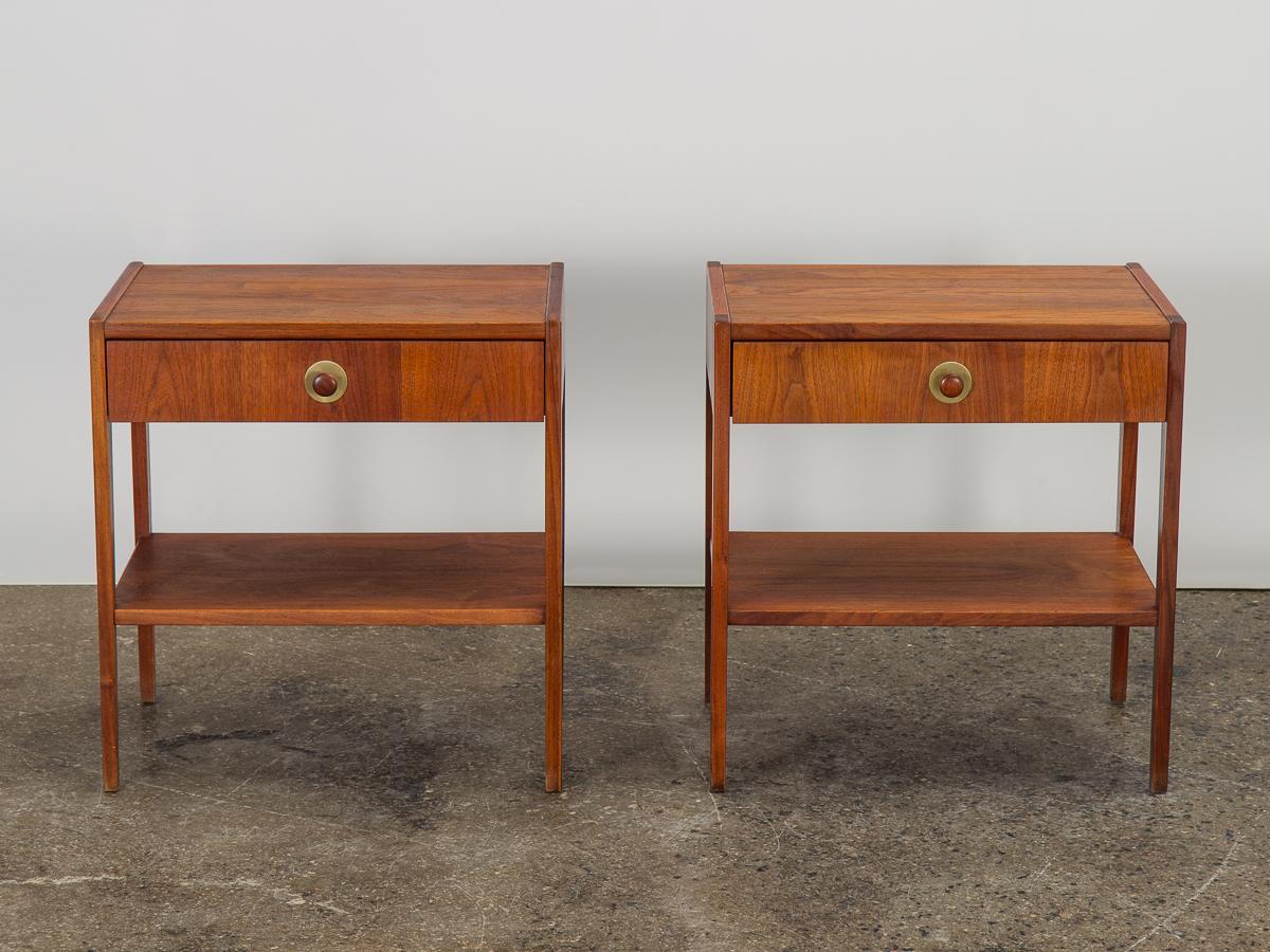 Pair of handsome Mid-Century Modern nightstands with minimal lines and nice details. Streamlined silhouette with lean, tapered legs. Drawers slide smoothly, finished with carved wooden knobs on a brushed brass disc. Pretty walnut wood selection is