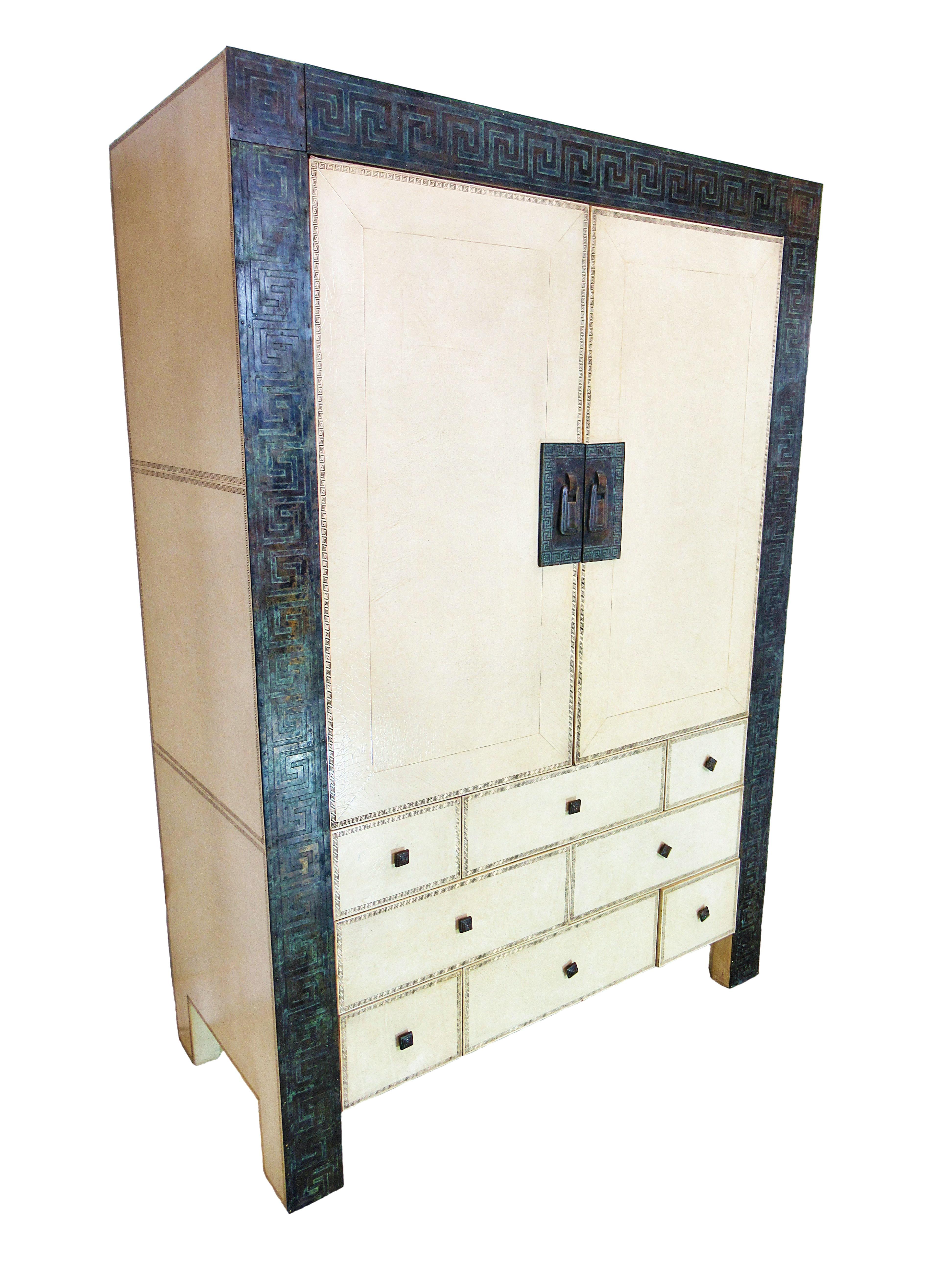 The piece overall in leather and parchment with fine gold embossing, the perimeter of the piece with applied bronze mouts with overall Greek key motif. The upper section with two doors revealing glass shelved areas for liquor and glass storage, the