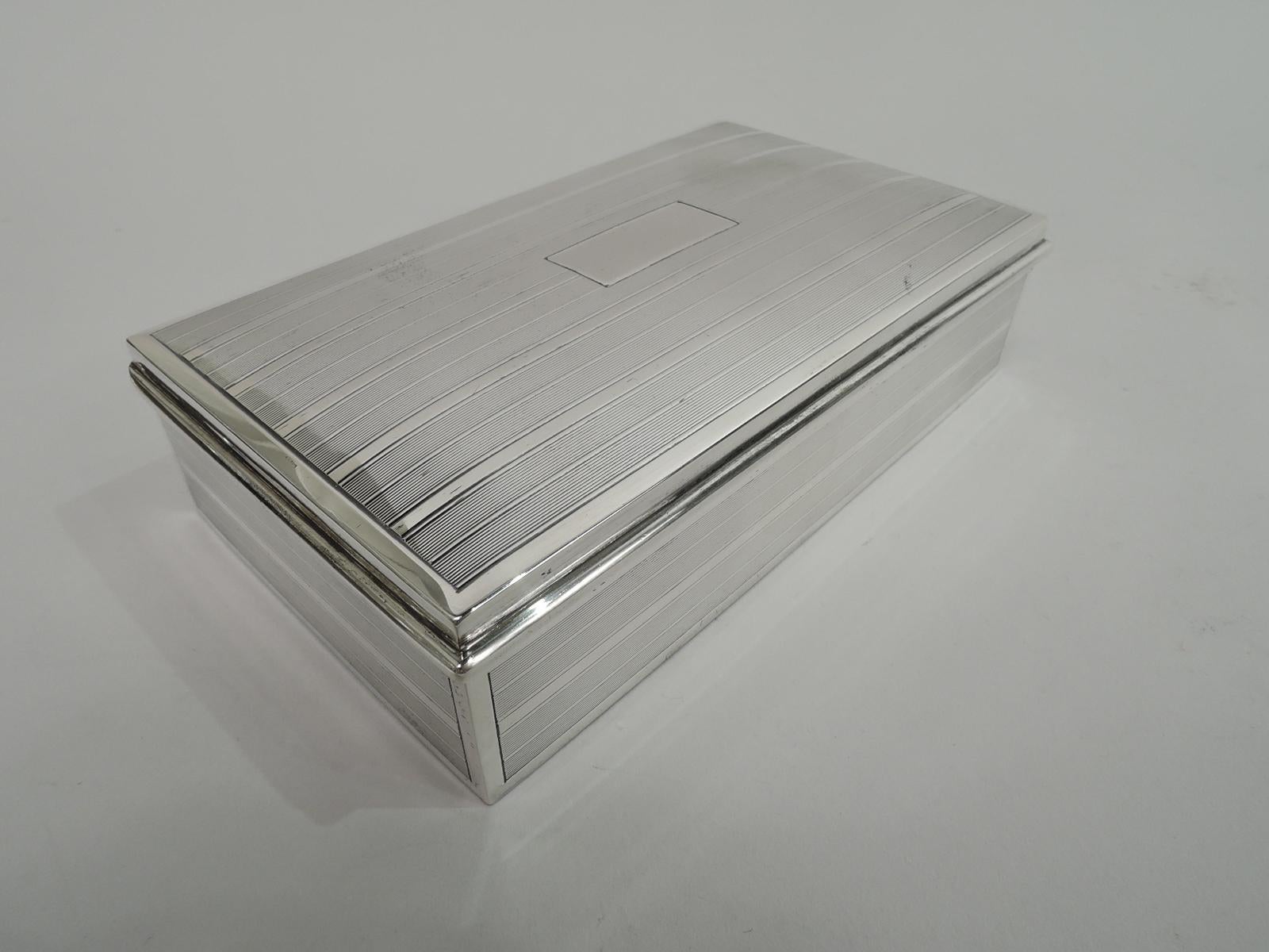 Modern sterling silver box. Made by Andrew A. Taylor in Newark, ca 1940. Rectangular with straight sides and crisp corners. Cover hinged with gently curved top and wraparound molded rim. Engine turned horizontal lines in plain frames on box sides