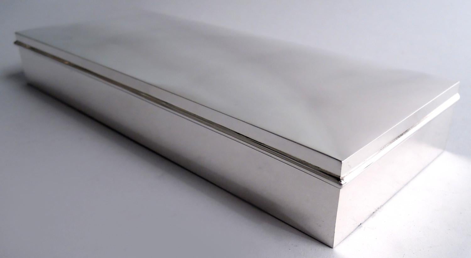 Moderna caja de plata de ley. Larga y rectangular, con lados rectos y esquinas afiladas; tapa articulada con borde saliente y parte superior suavemente curvada. Interior de la caja forrado de cedro y tabicado. Cubierta interior dorada. Bonitas