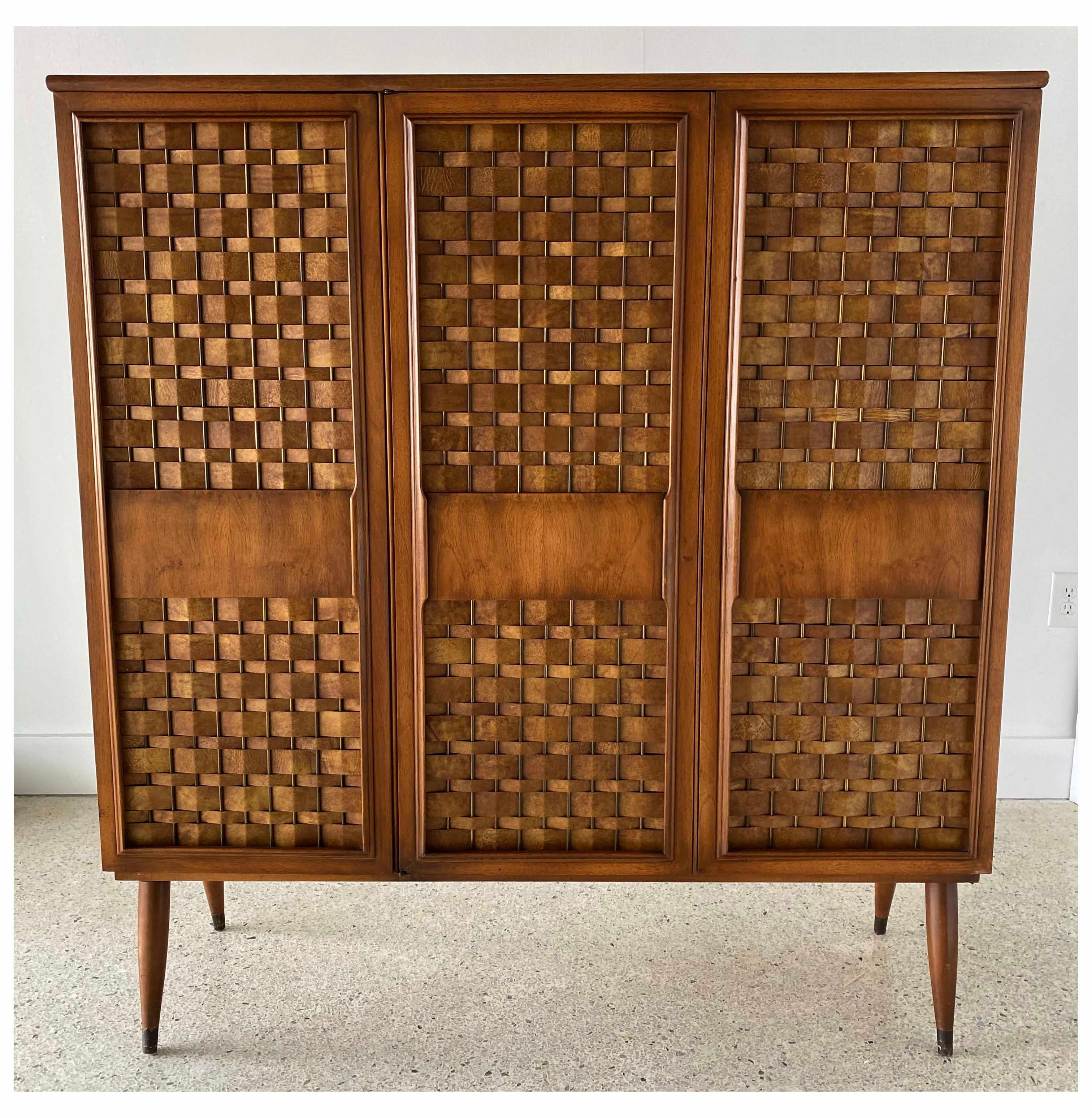 American modern upright 3 door cabinet by Dunbar. This cabinet features 2 storage sections comprised of three doors, each with capacity for 3 shelves. 
The cabinet has a shallow profile of 14
