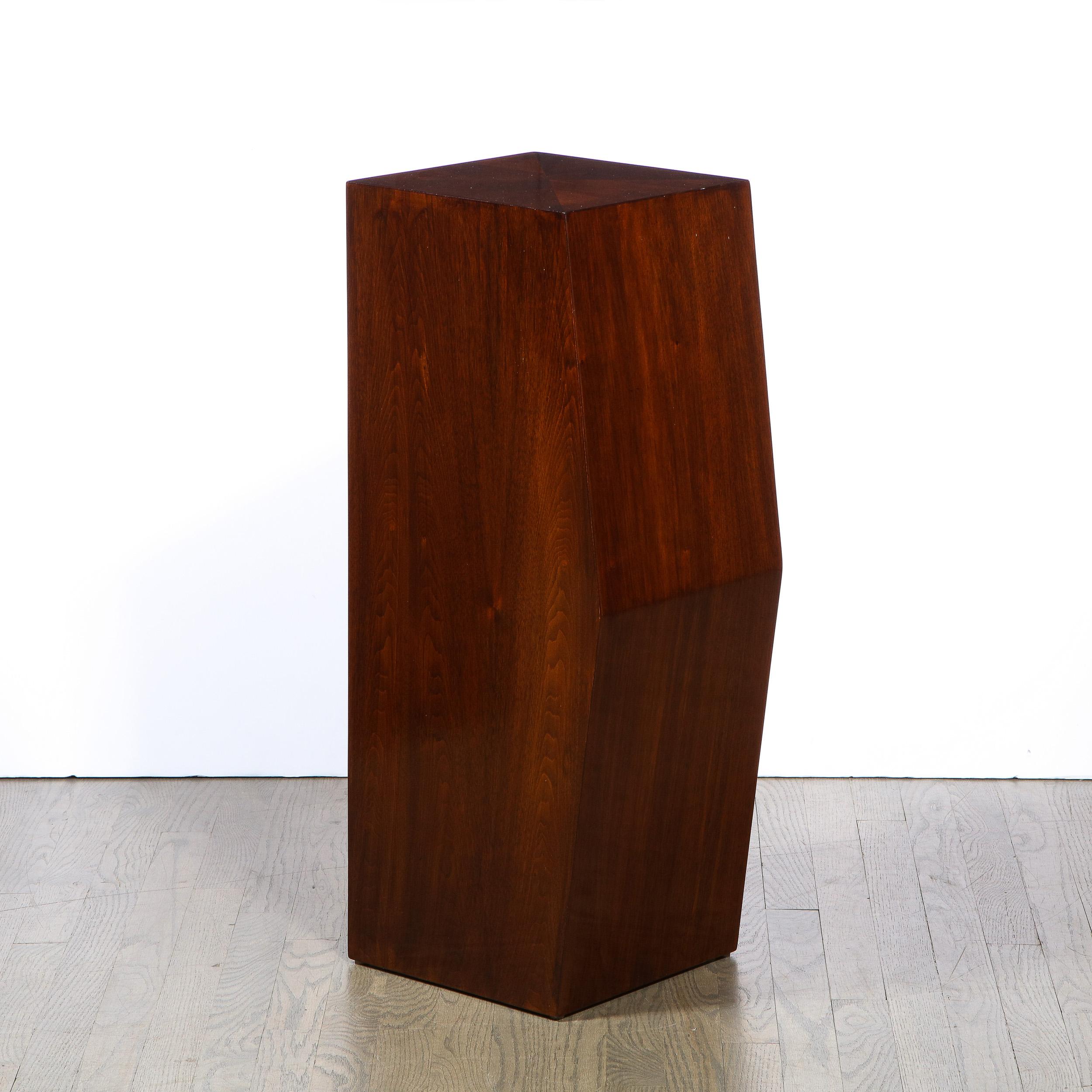 This elegant modernist pedestal was realized in the United States during the latter half of the 20th century. It Composed of bookmatched walnut, the pedestal offers a minimalist and austere volumetric rectangular form with one side that protrudes