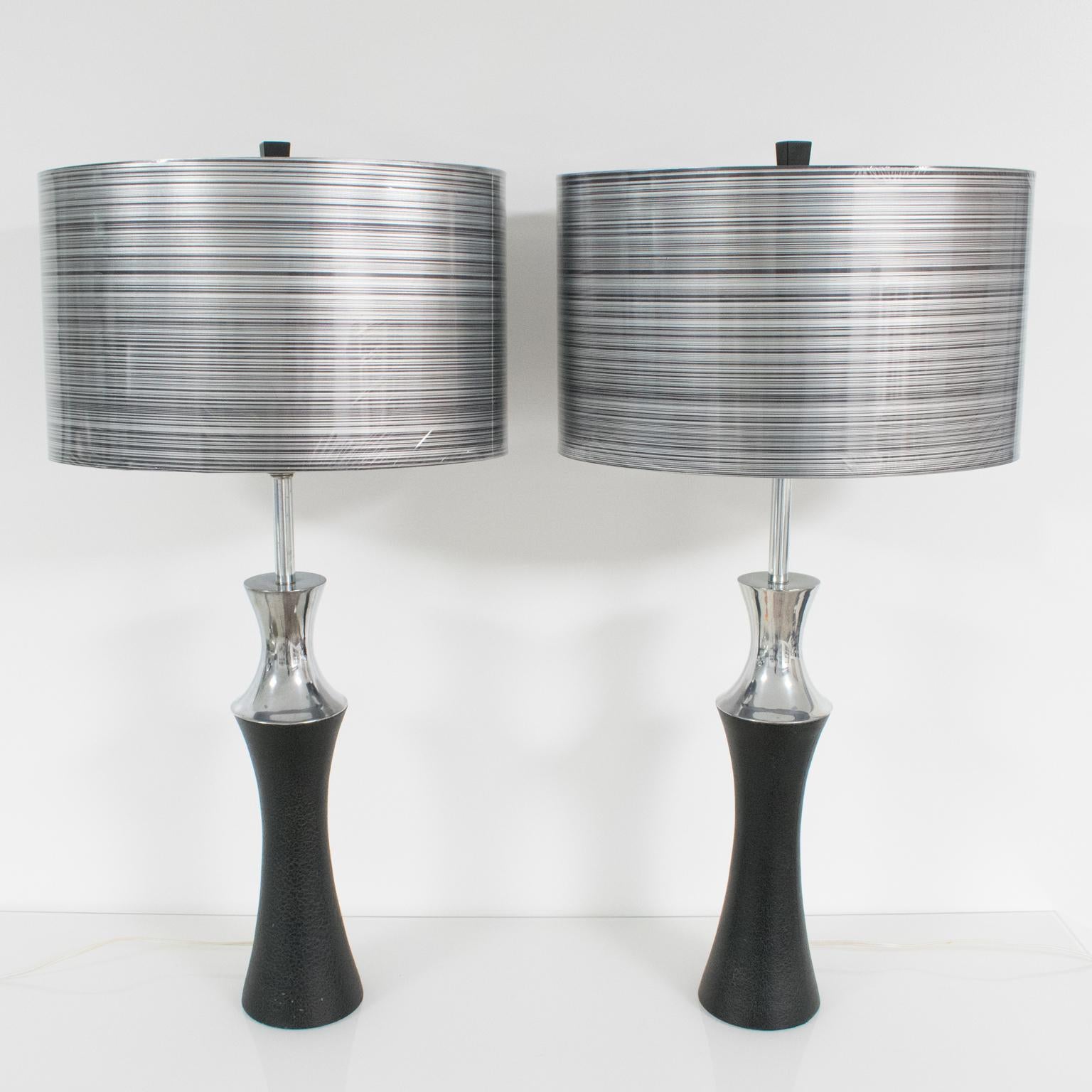 This pair of table lamps, designed by Mutual Sunset Lamp Co, Brooklyn, NY, boasts a modernist Machine Age shape with polished cast aluminum and black painted metal with a textured pattern. The lamps are paired with modern oval rhodoid shades