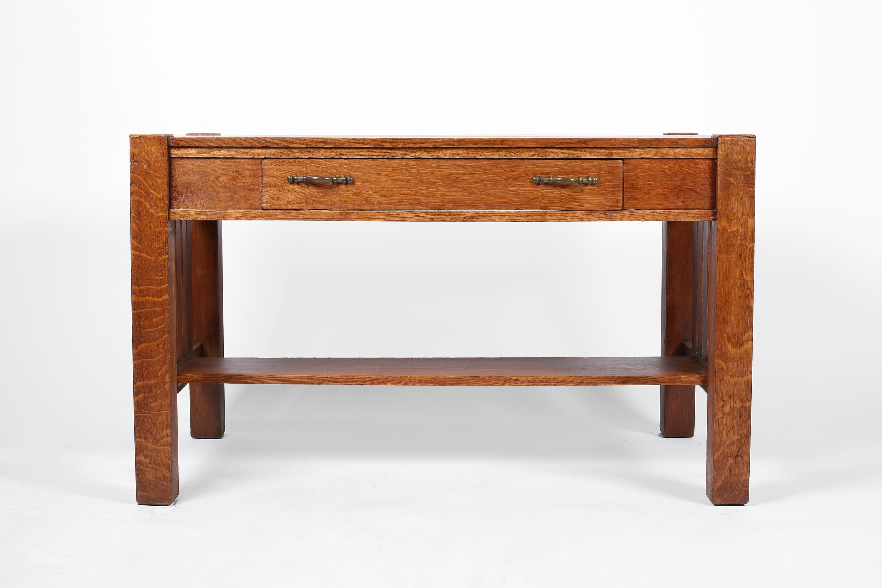 A fine solid oak Arts & Crafts desk in the manner of Frank Lloyd Wright. Featuring a planked top with cubic, column-esque legs and slatted side detailing. The brass drawer pulls a later, but more than suitable, replacement for the originals. Honeoye