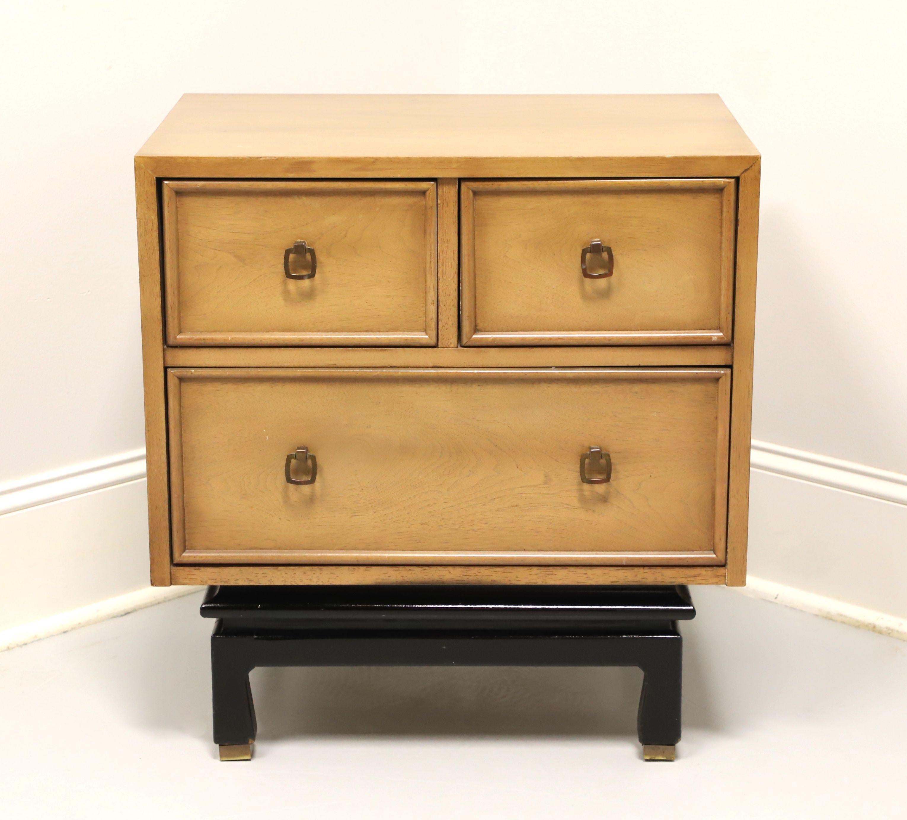 An Asian inspired three-drawer nightstand by American of Martinsville. Walnut with a light blonde finish, smooth top, brass hardware, black painted slightly raised base on four legs with base caps. Features two smaller drawers over one larger