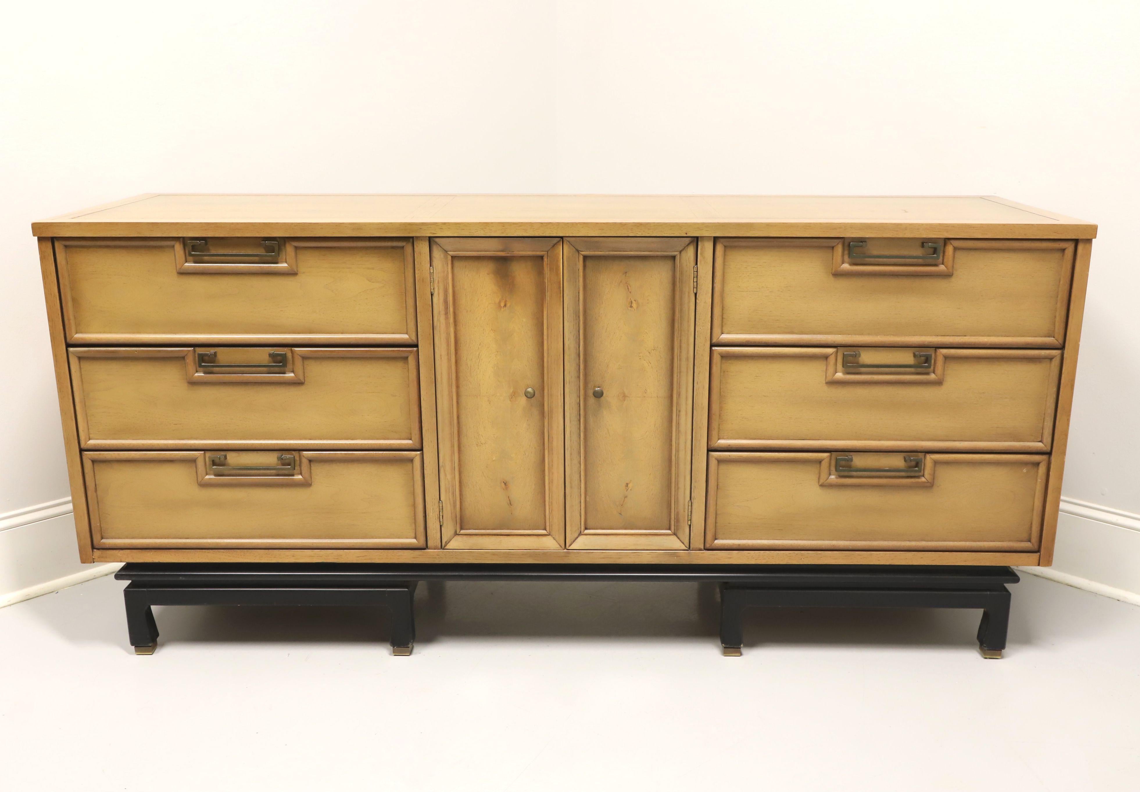 An Asian inspired triple dresser by American of Martinsville. Walnut with a light blonde finish, banded top, brass hardware, black painted slightly raised base on eight legs with base caps. Features a center two door cabinet revealing three smaller