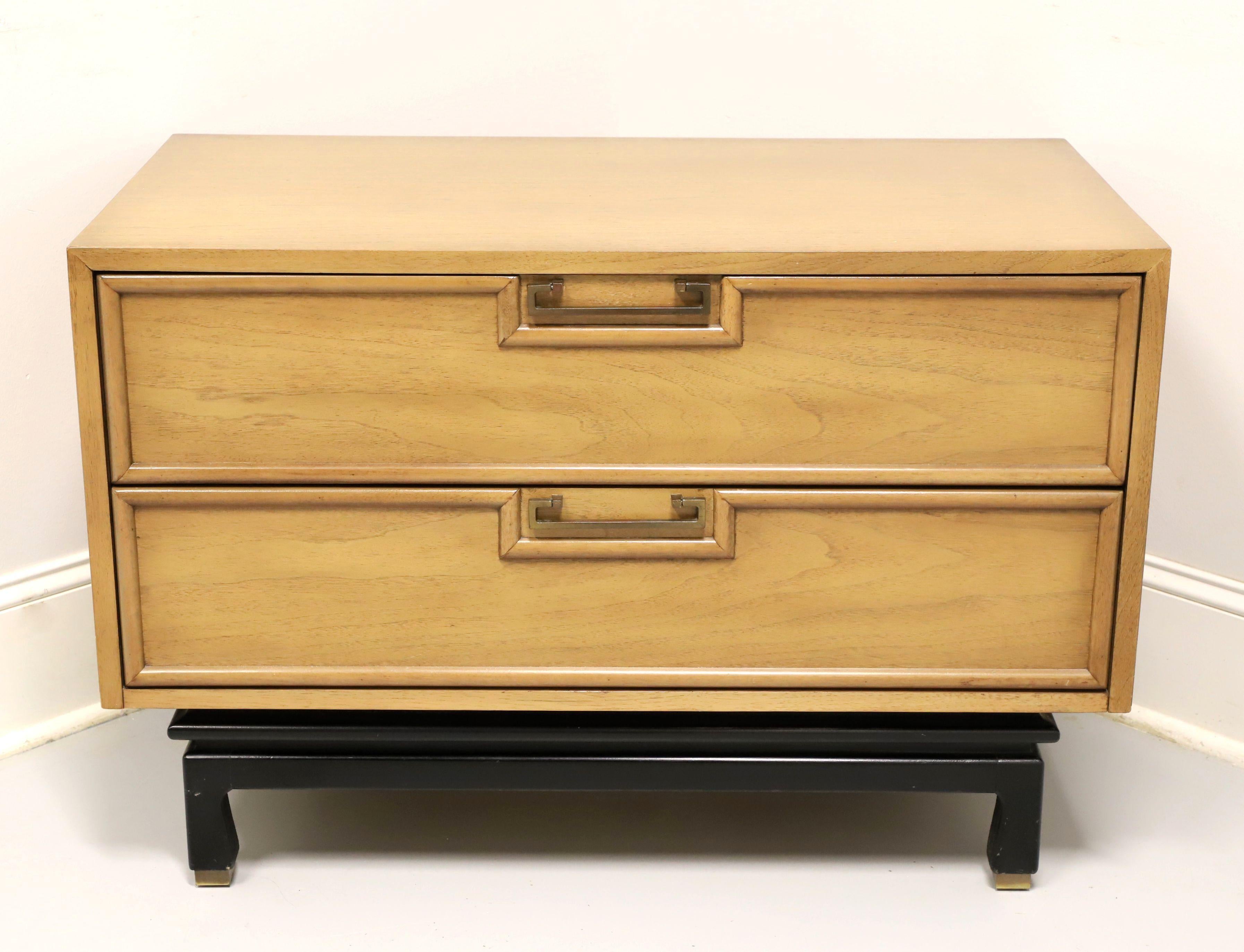 An Asian inspired two-drawer nightstand by American of Martinsville. Walnut with a light blonde finish, smooth top, brass hardware, black painted slightly raised base on four legs with base caps. Features two drawers of dovetail construction, top