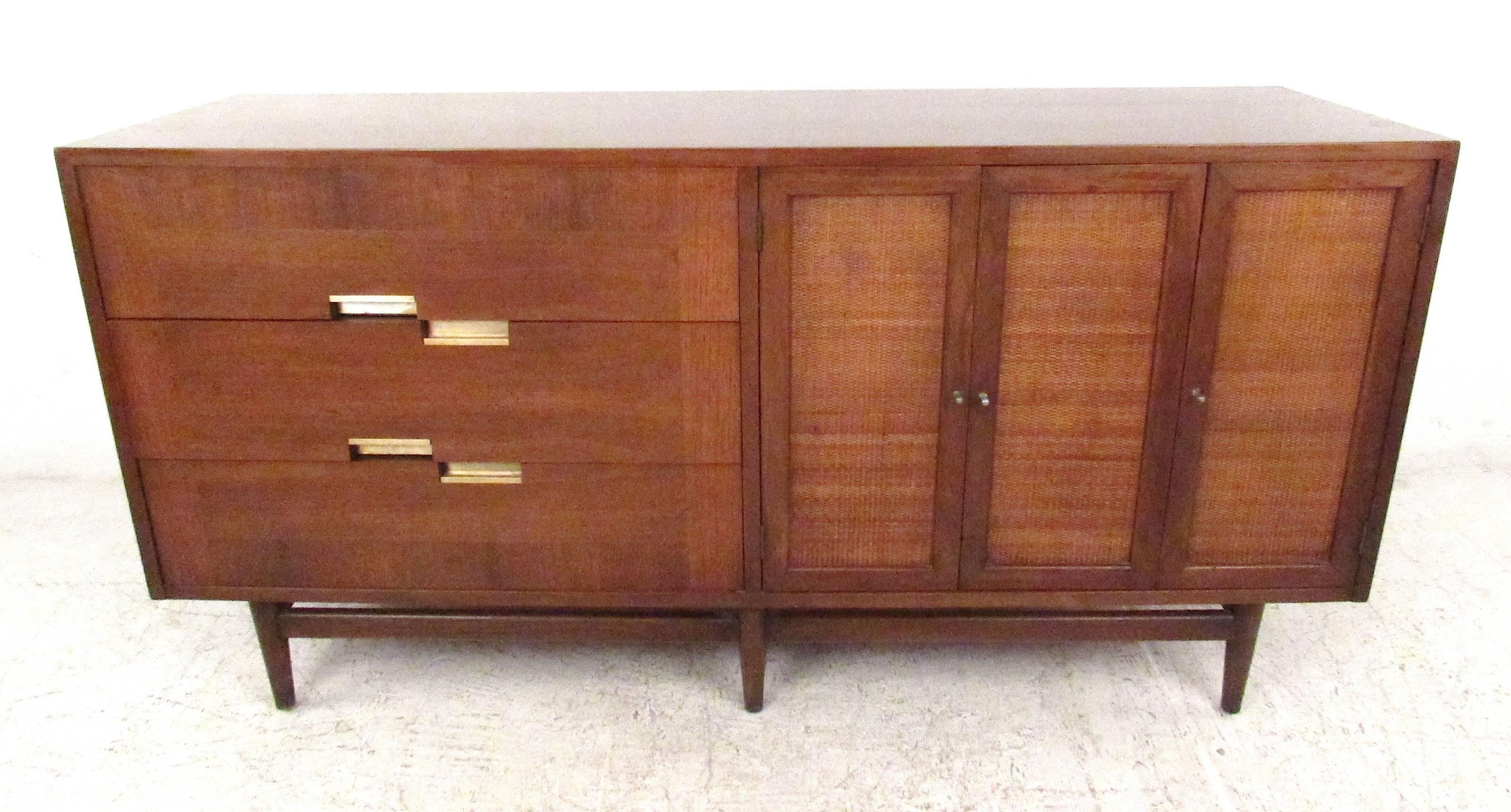 Beautiful American of Martinsville credenza featuring walnut top with x-shaped ornamental inlays in brushed aluminum and three cane front doors which open to drawers and storage compartments. On the left side are three dovetailed drawers with