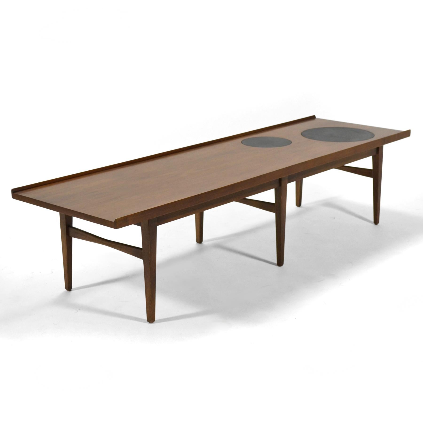 This fantastic walnut coffee table by American of Martinsville has several nice details. It has bow tie shaped stretchers, raised edges on the sides, and two circular mica inserts in the top.