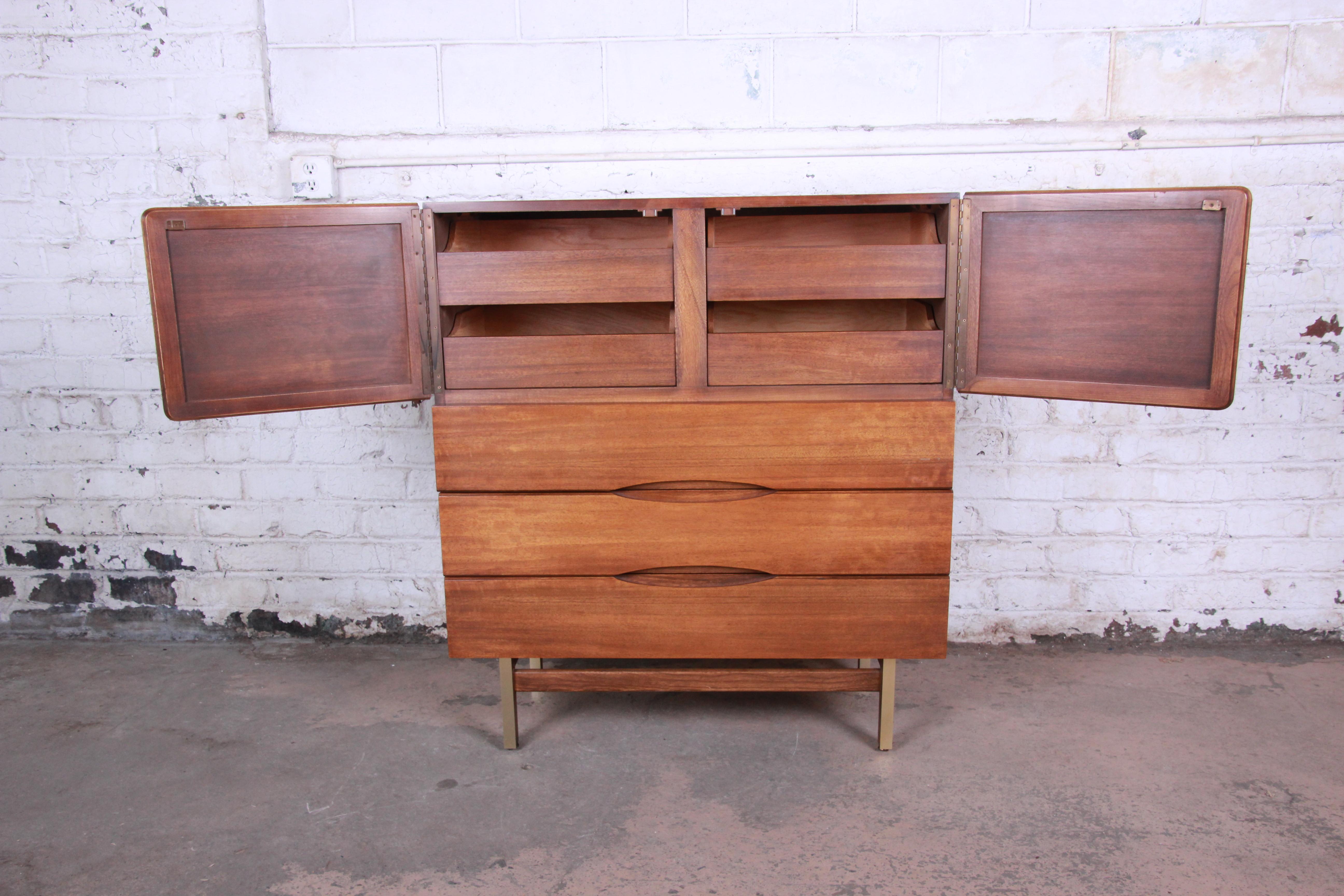 A very nice Mid-Century Modern walnut gentleman's chest by American of Martinsville. The dresser features gorgeous walnut wood grain, with brass-trimmed legs. It offers ample room for storage, with four drawers behind two woven-front doors at the