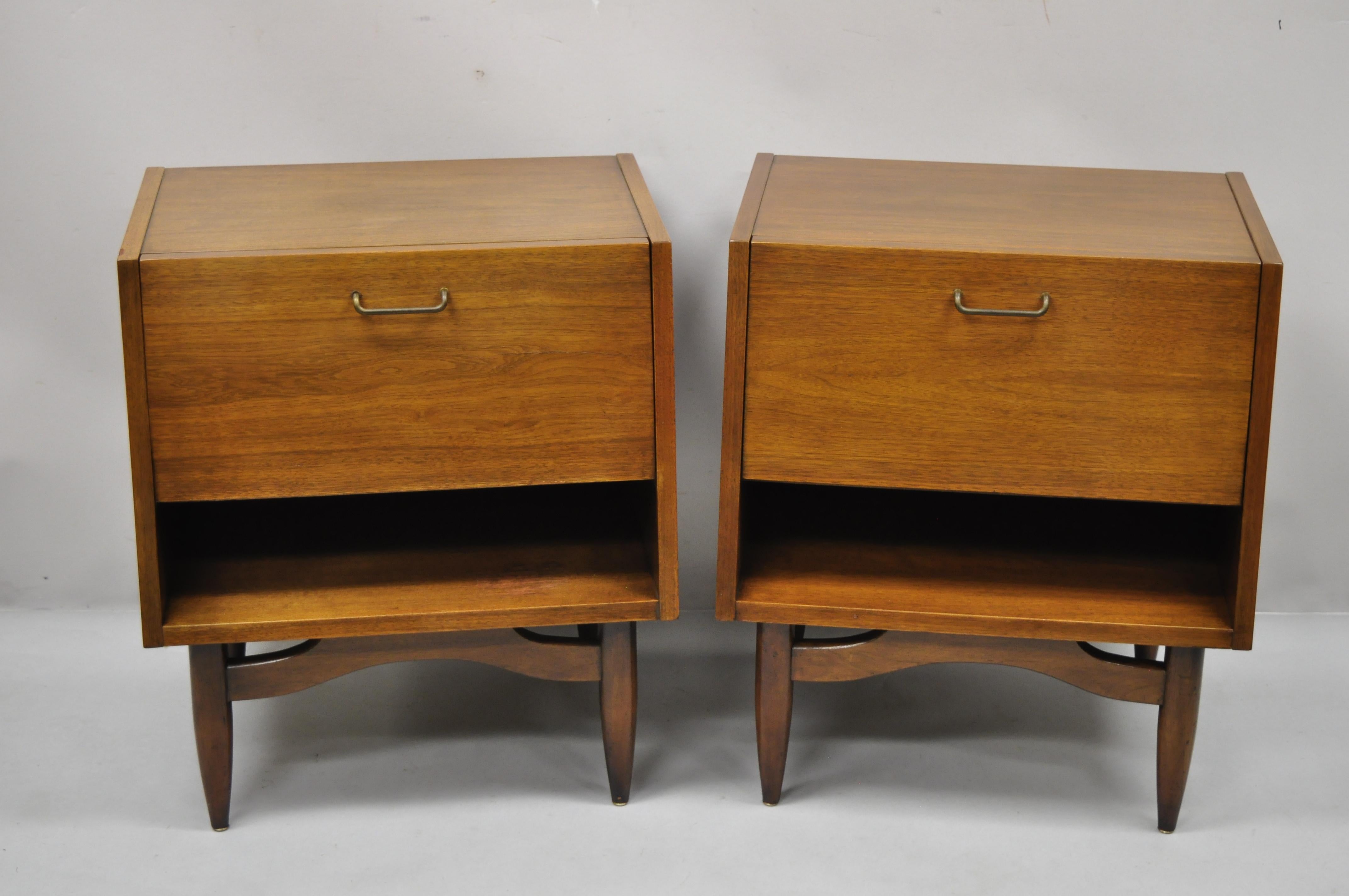 American of Martinsville Mid-Century Modern walnut nightstands bedside tables, a pair. Item features 1 fall front door, storage cubby interior, laminate surface, beautiful wood grain, original stamp, 1 dovetailed drawer, tapered legs, very nice
